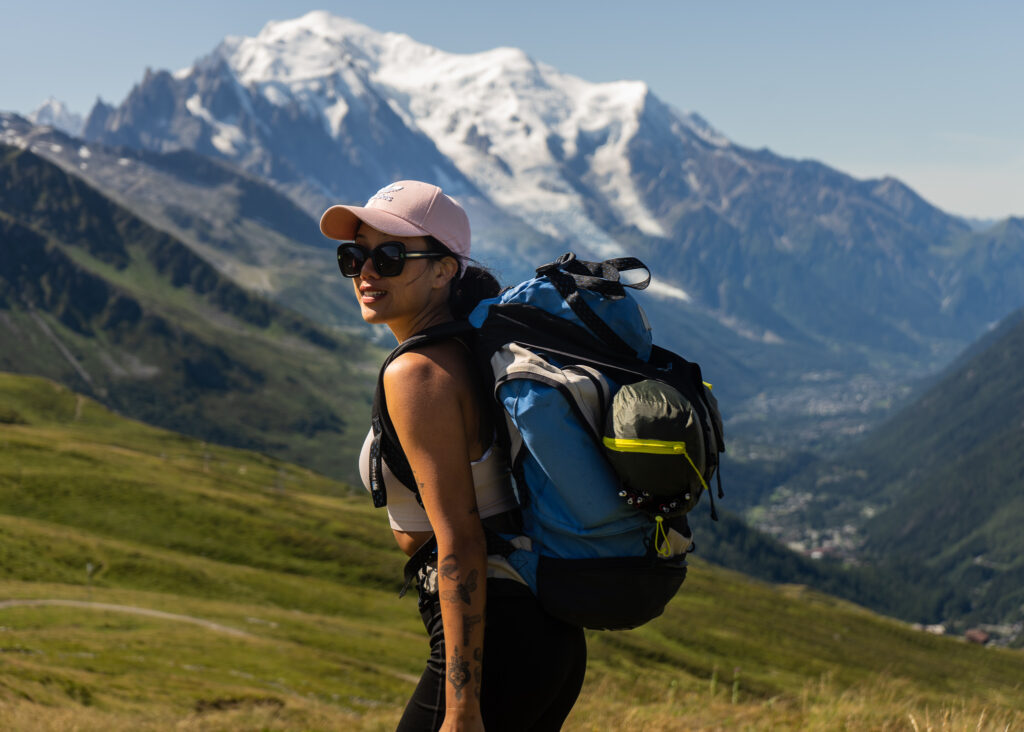 a girl with a backpack in the swiss alps in summer. backpacking and hiking are free activities to lower the cost to travel for a year