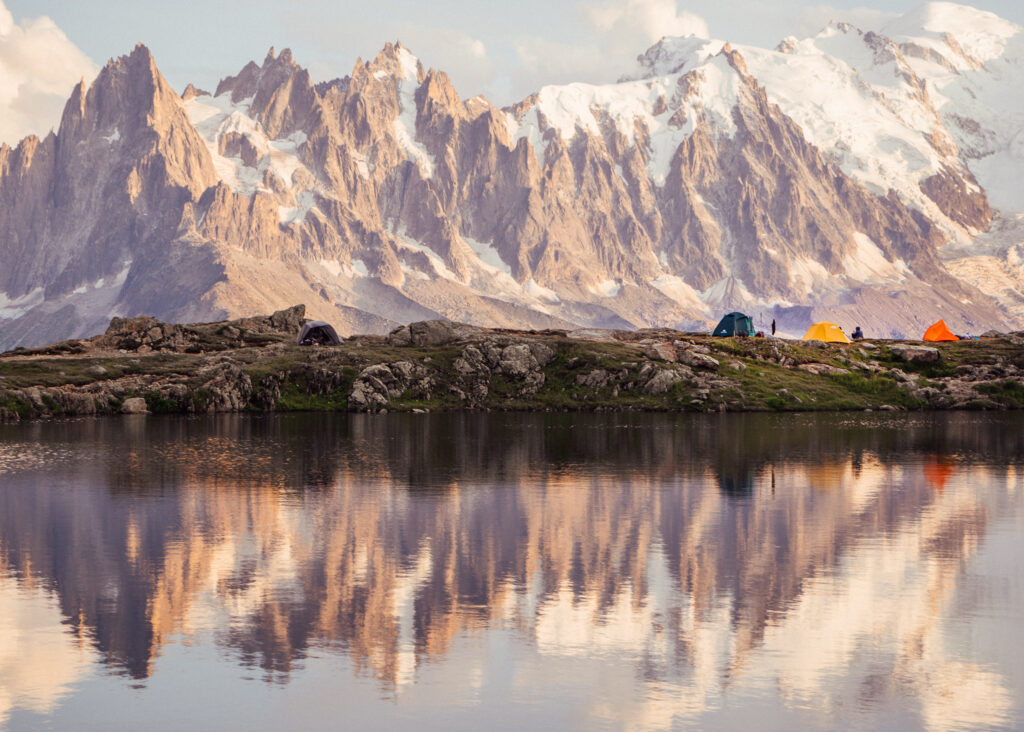 camping in the french alps in summer next to a lake at sunset with the snowy mountains in the back. camping is free and a good activity to lower the cost to travel for a year