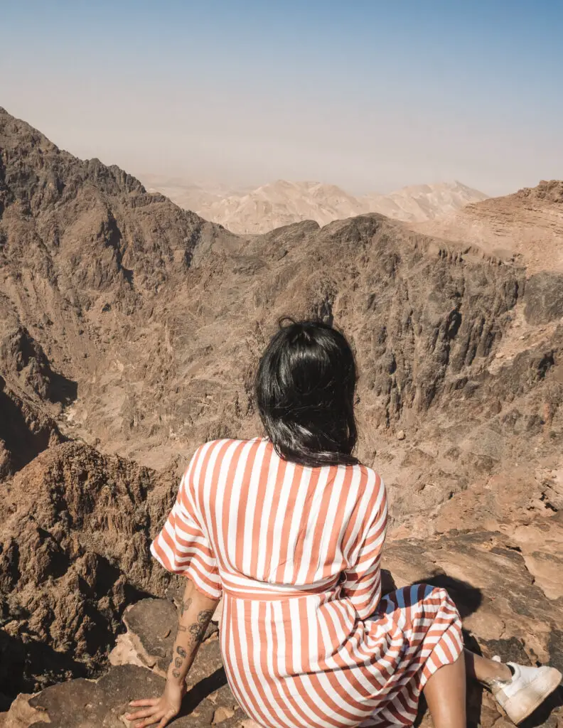 a girl looking over a cliff to the canyon below in petra in jordan