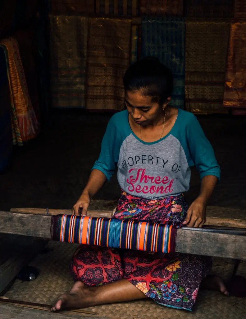 local woman in lombok making handmade goods and clothing using colorful thread on the floor in a dark hut