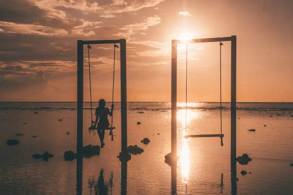 a girl on a swing over the ocean at sunset on the gili trawangan island