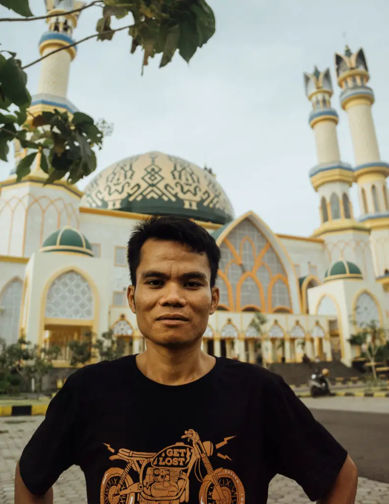 an indonesian man in front of a large green and gold mosque on lombok island on a sunny day