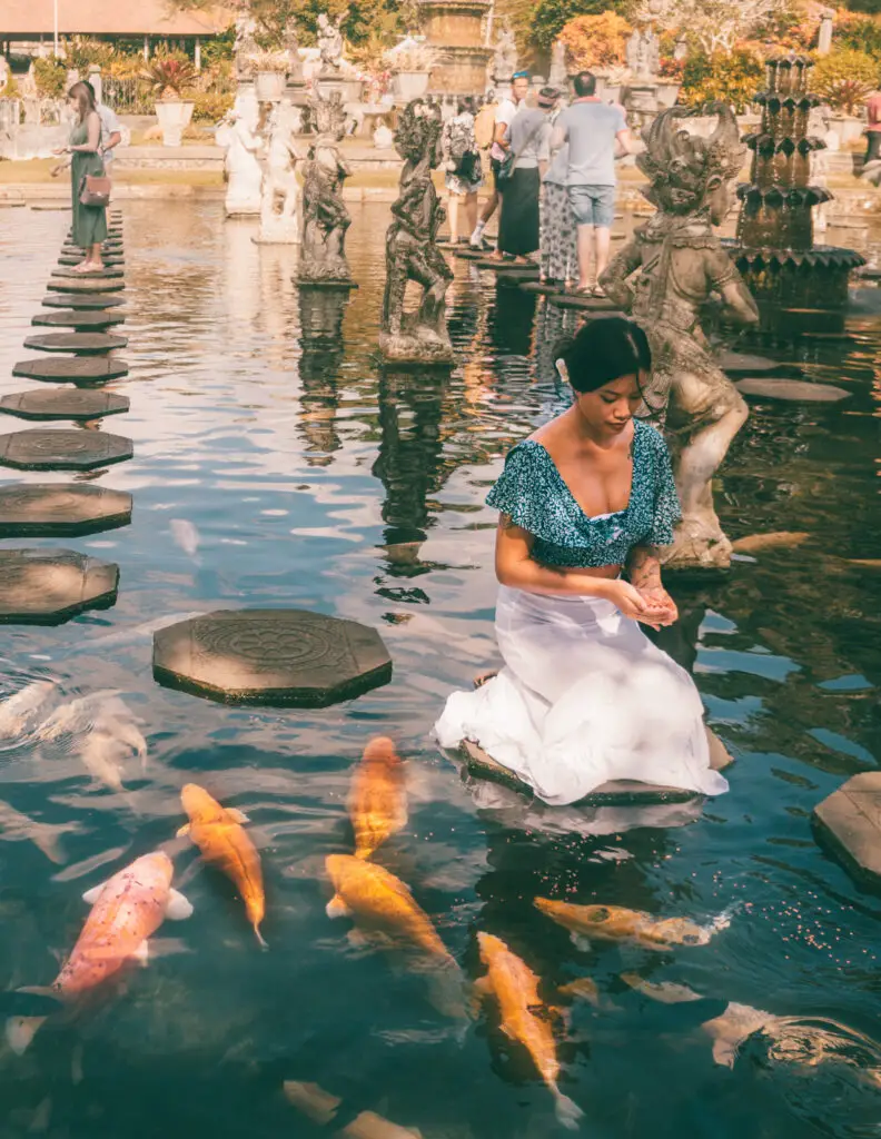 a girl feeding koi fish in a pond at a balinese temple called tirta gangga in bali