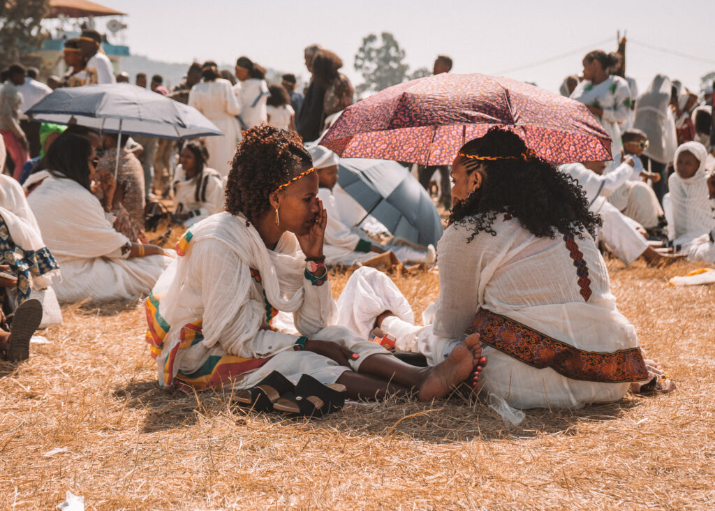 two women sitting in the grass wearing traditional ethiopian clothing during timkat in addis ababa