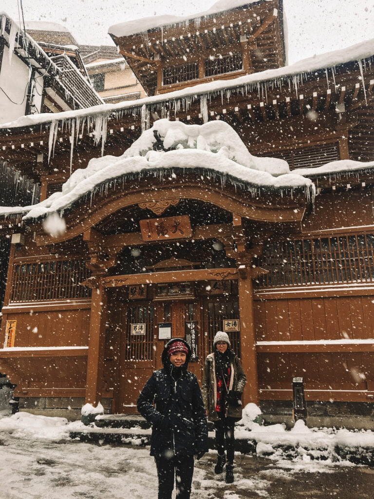 two girls in the snow outside an onsen in nozawa in japan