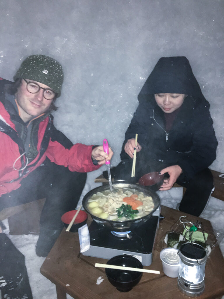 a man and woman eating japanese hot pot inside an igloo in japan