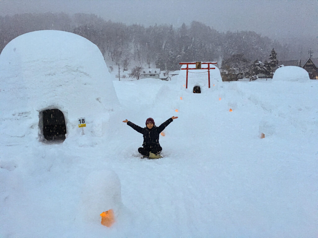 a girl sitting in the snow next to some igloos in japan
