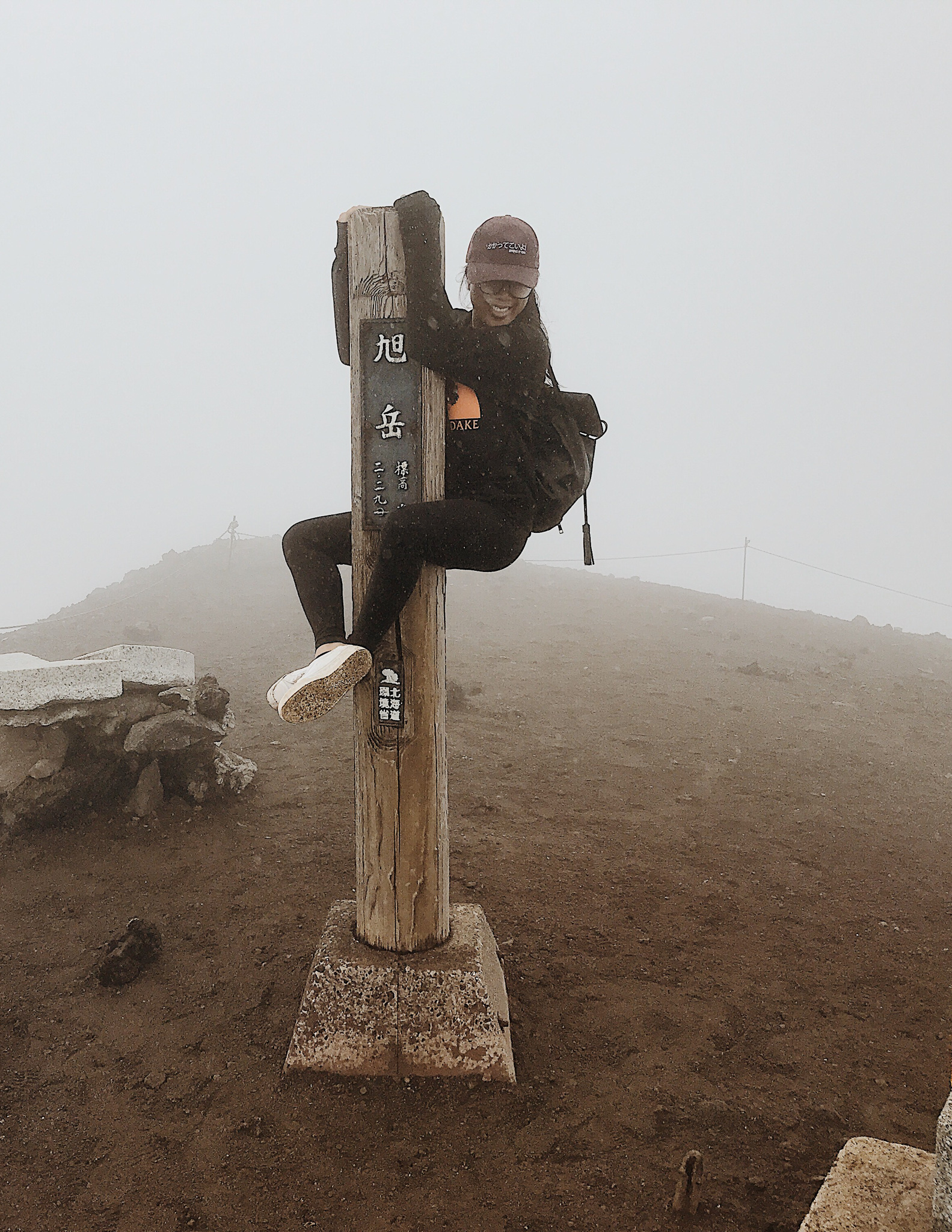 A girl climbing a pole at the summit of Mt. Asahidake in summer