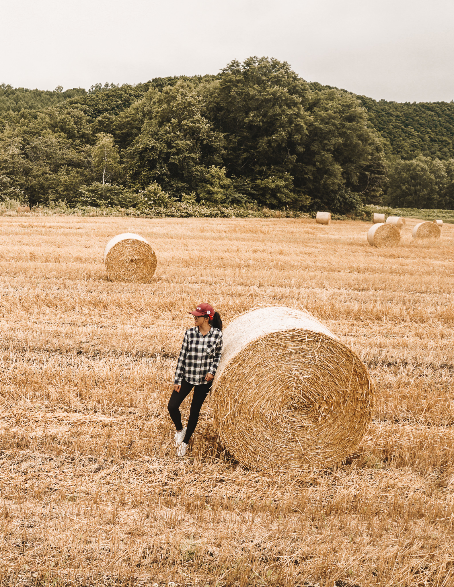 A woman leaning up against a circular hay barrel in Hokkaido in summer