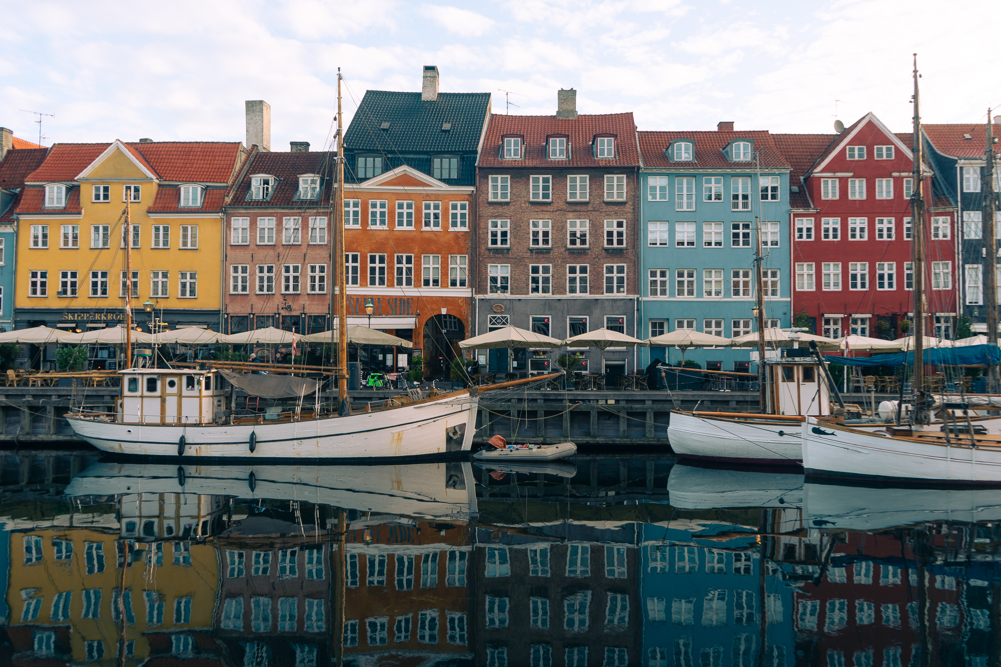 red, blue, orange and yellow fisherman houses with some sailboats parked in front in a canal in Copenhagen