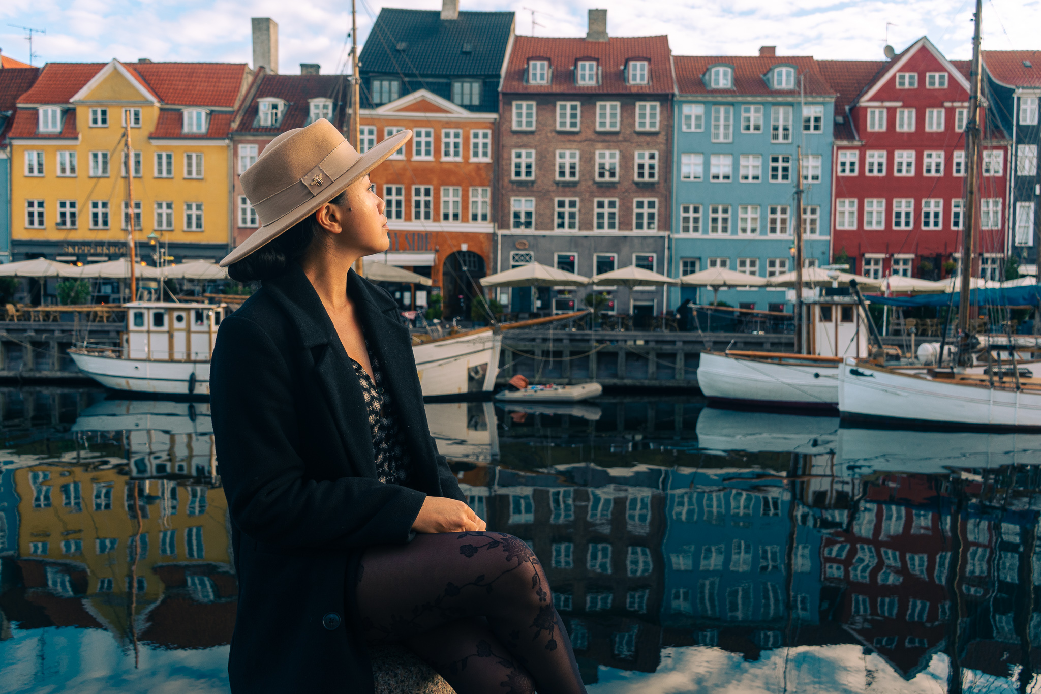 A woman sitting next to the canal in Nyhavn, Copenhagn, in front of the historic colorful fishermen houses