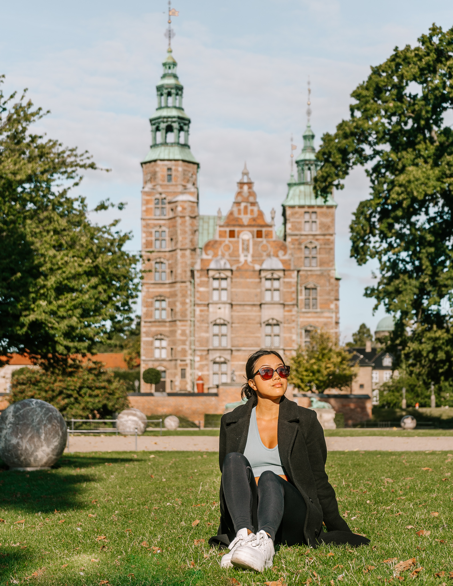 A woman sitting on the grass on a sunny day in the park in front of Rosenburg Castle in Copenhagen.