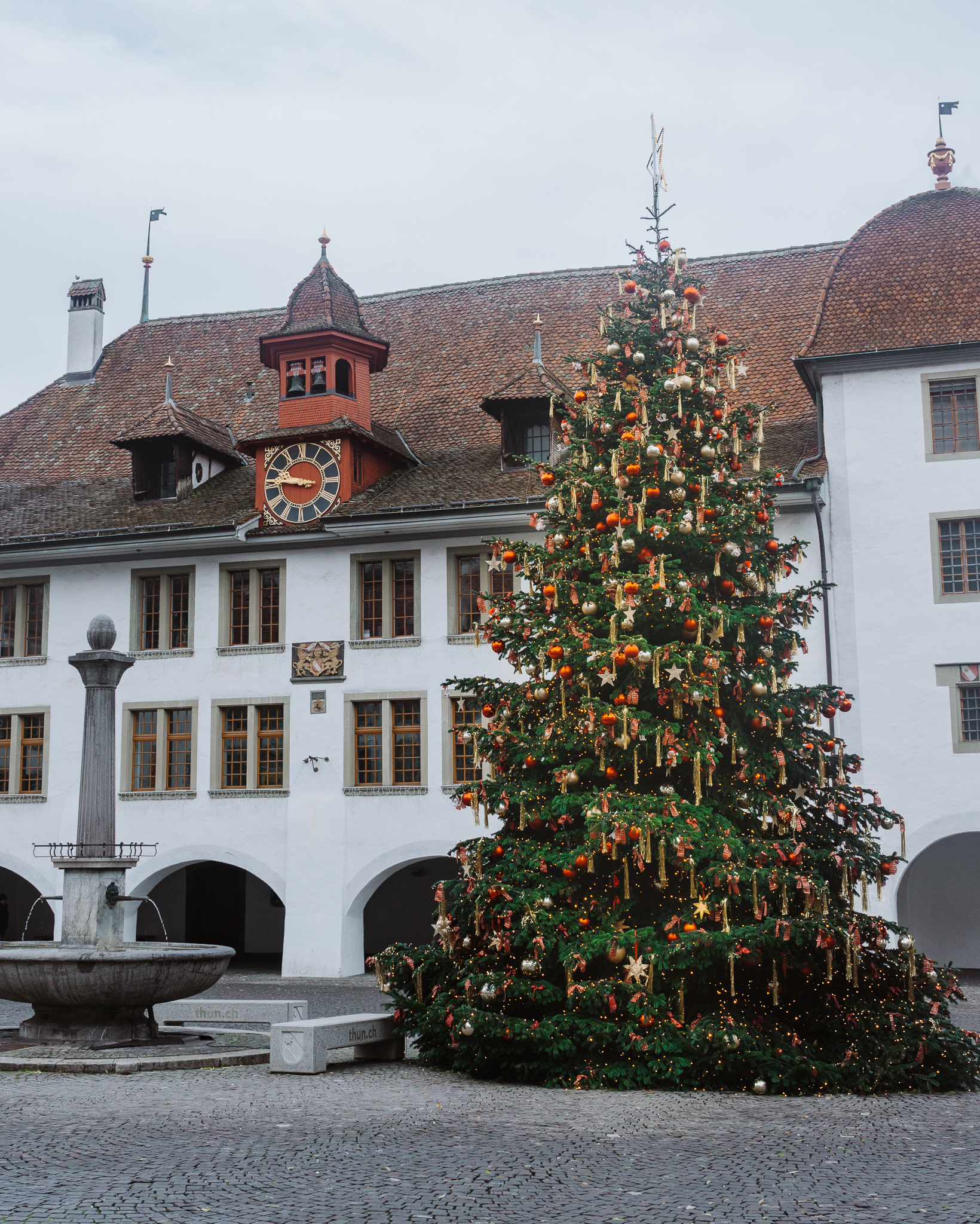 A large Christmas tree extravagantly decorated with stars and red baubles, in front if a historic Swiss building with a clock on it.