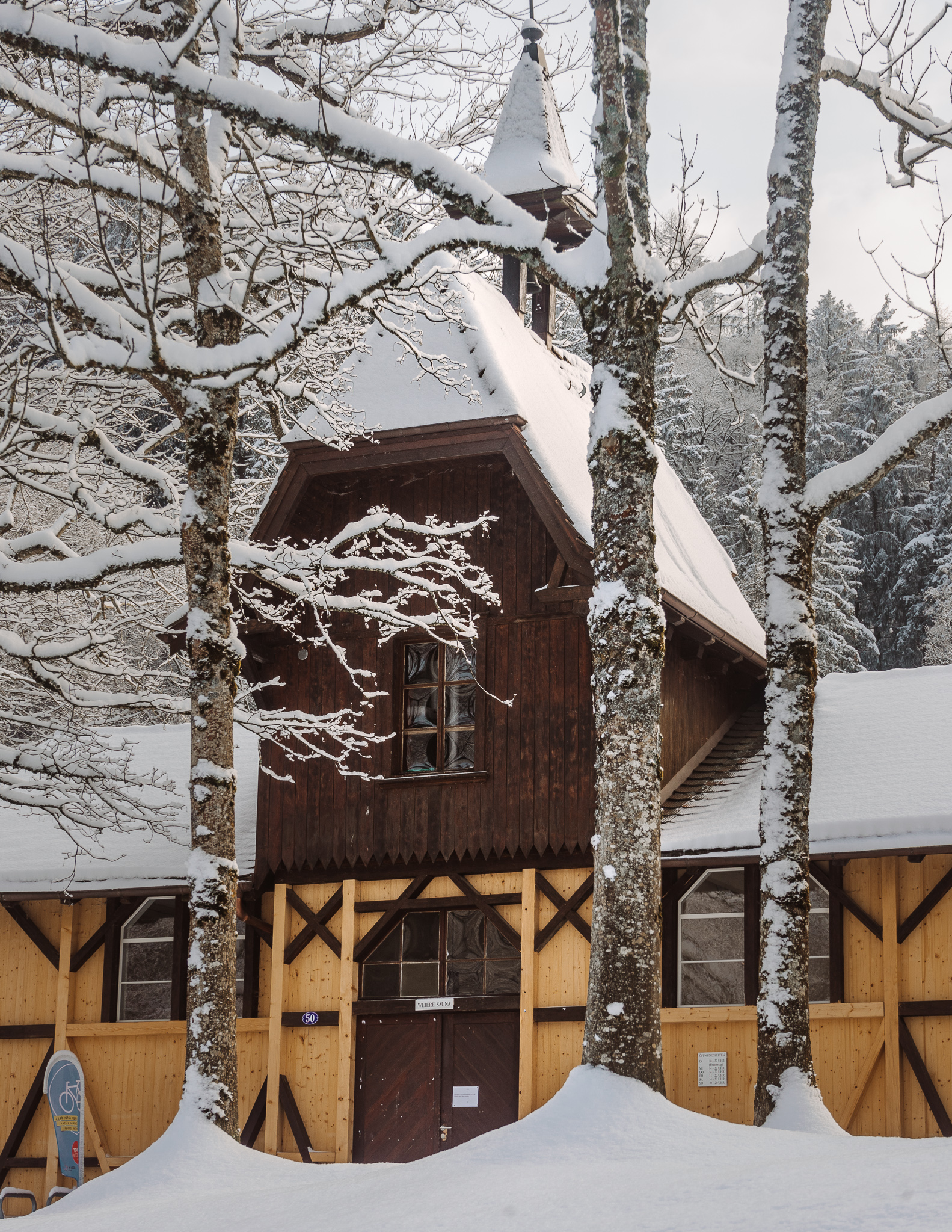 The Weiere Sauna, a wooden structure in the forest with snow on the roof and surrounding trees.