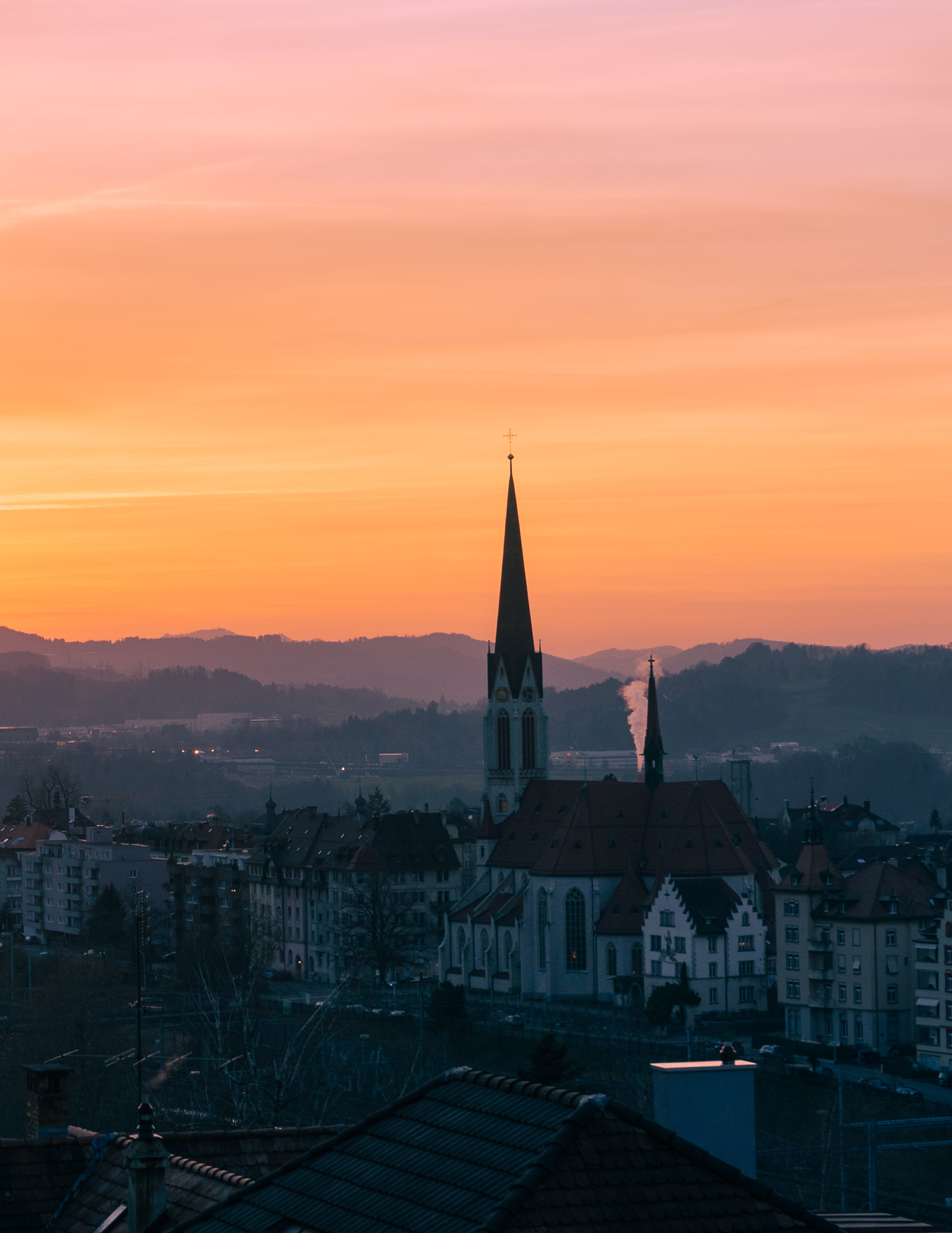 a pink and orange sunset in st. gallen in winter , with a view of the church spire in shadows.