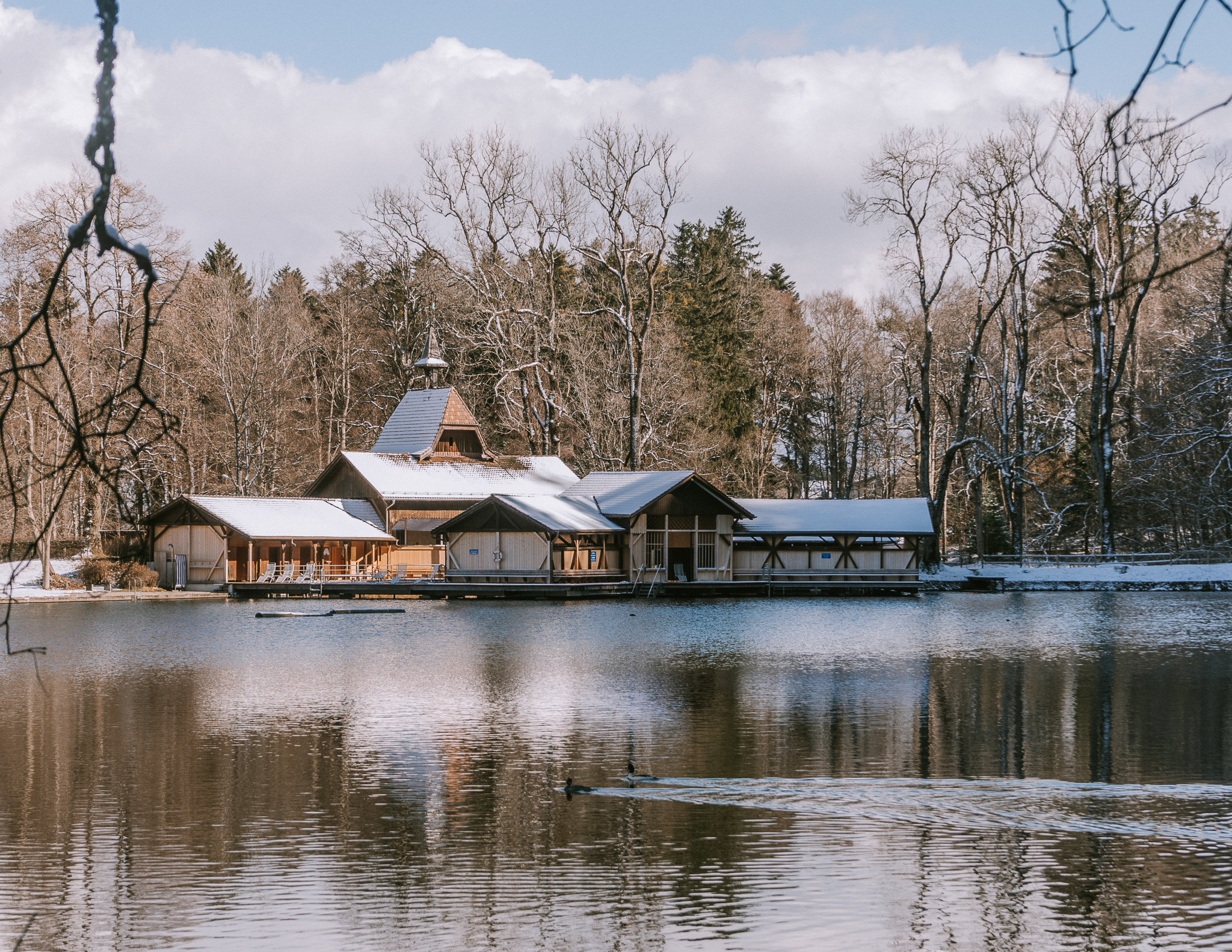 a view of the Weiere Sauna from the lake in winter, with snow on the roof and trees.