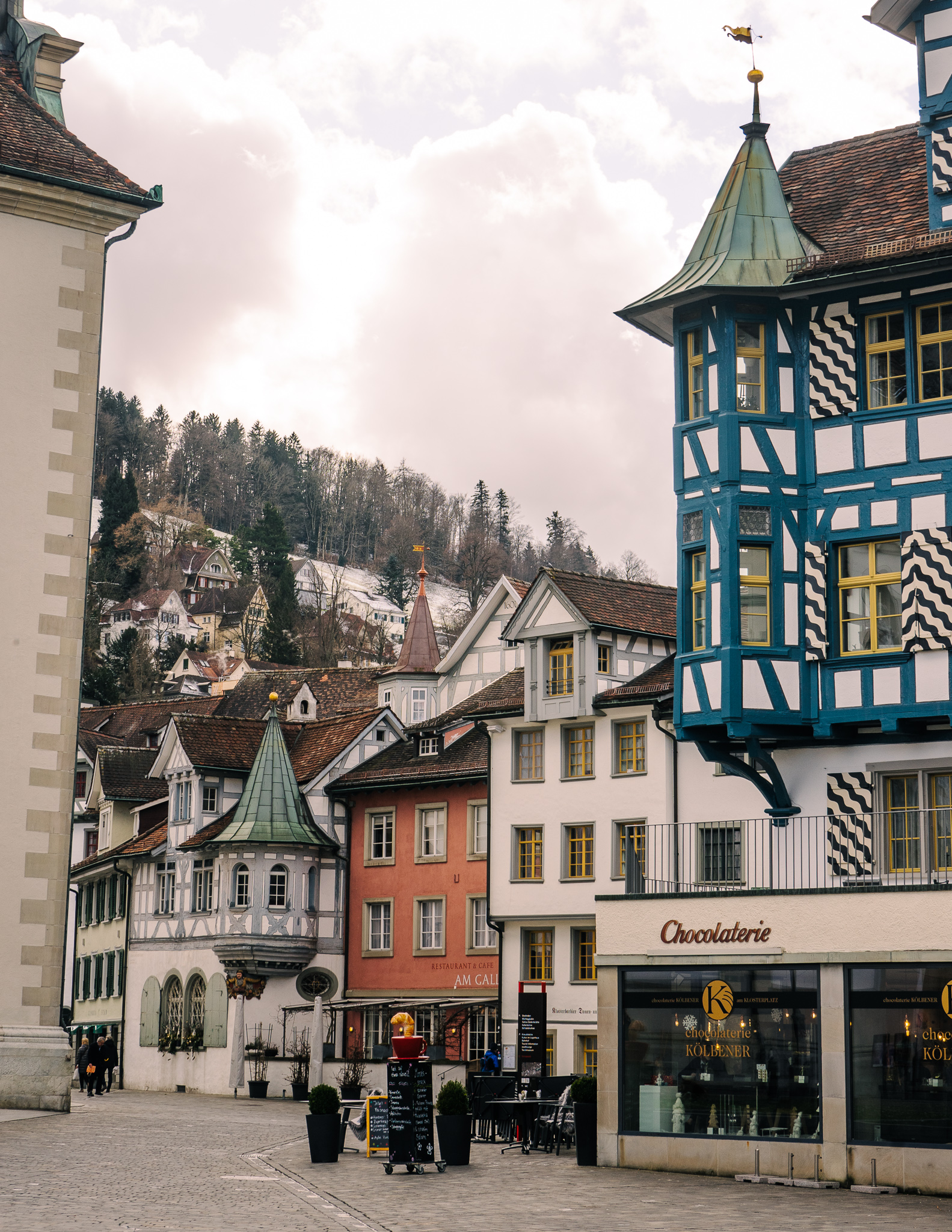 View of the old town buildings in St. Gallen in winter with a view of the snowy hills and trees behind.