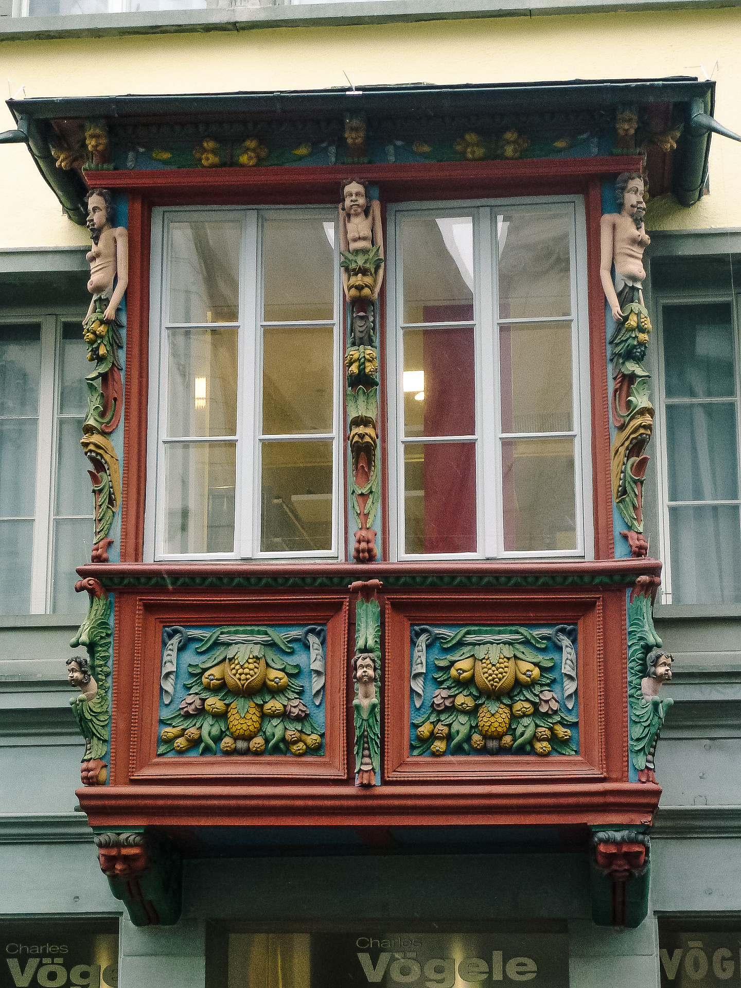 close up view of an intricately carved window in St. Gallen. It's colorful, and features flowers, fruit and cherubs.