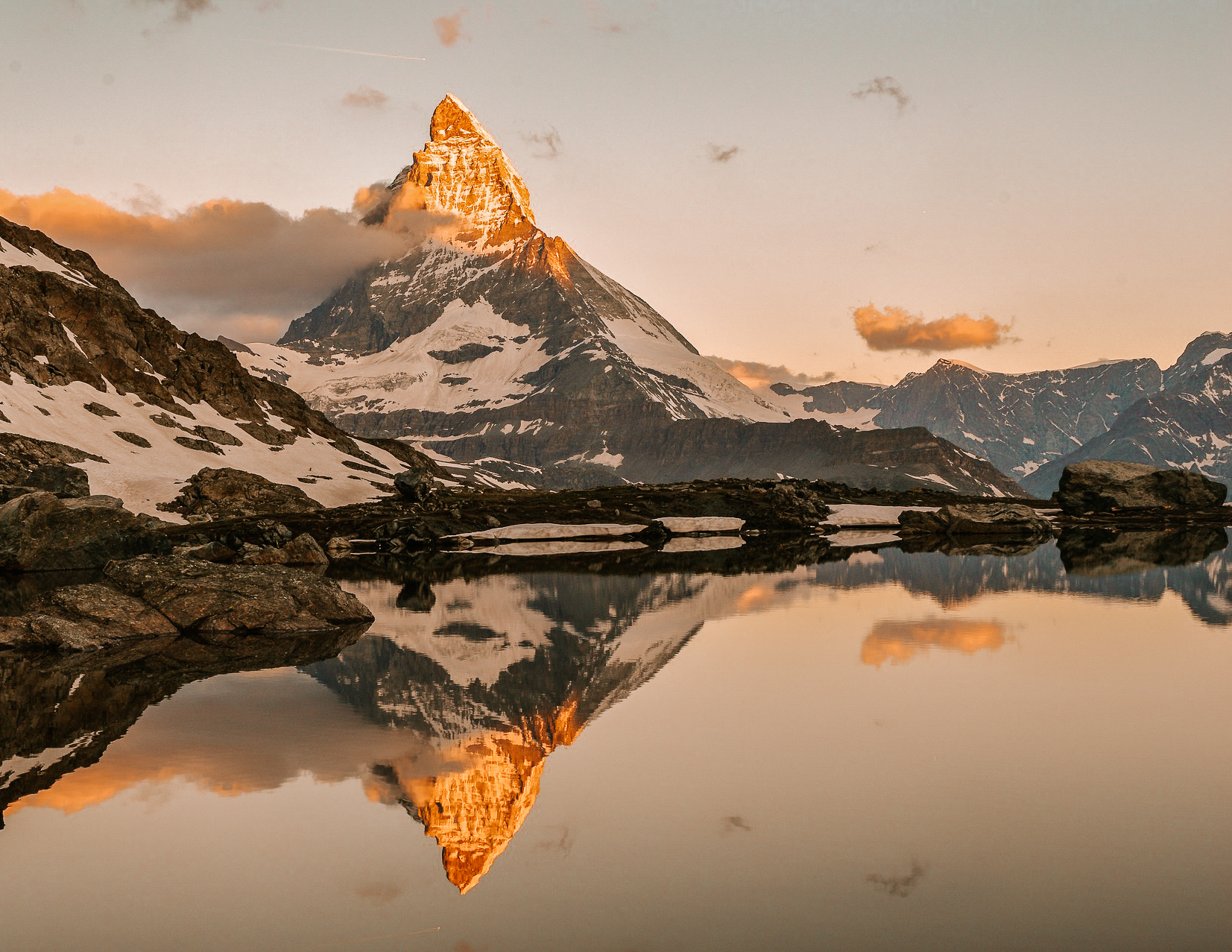 view of the Matterhorn near zermatt at sunrise above a lake with a perfect reflection on the lake surface. There is snow on Materhorn and the foreground, and the tip of Matterhorn is reflecting golden sunlight.