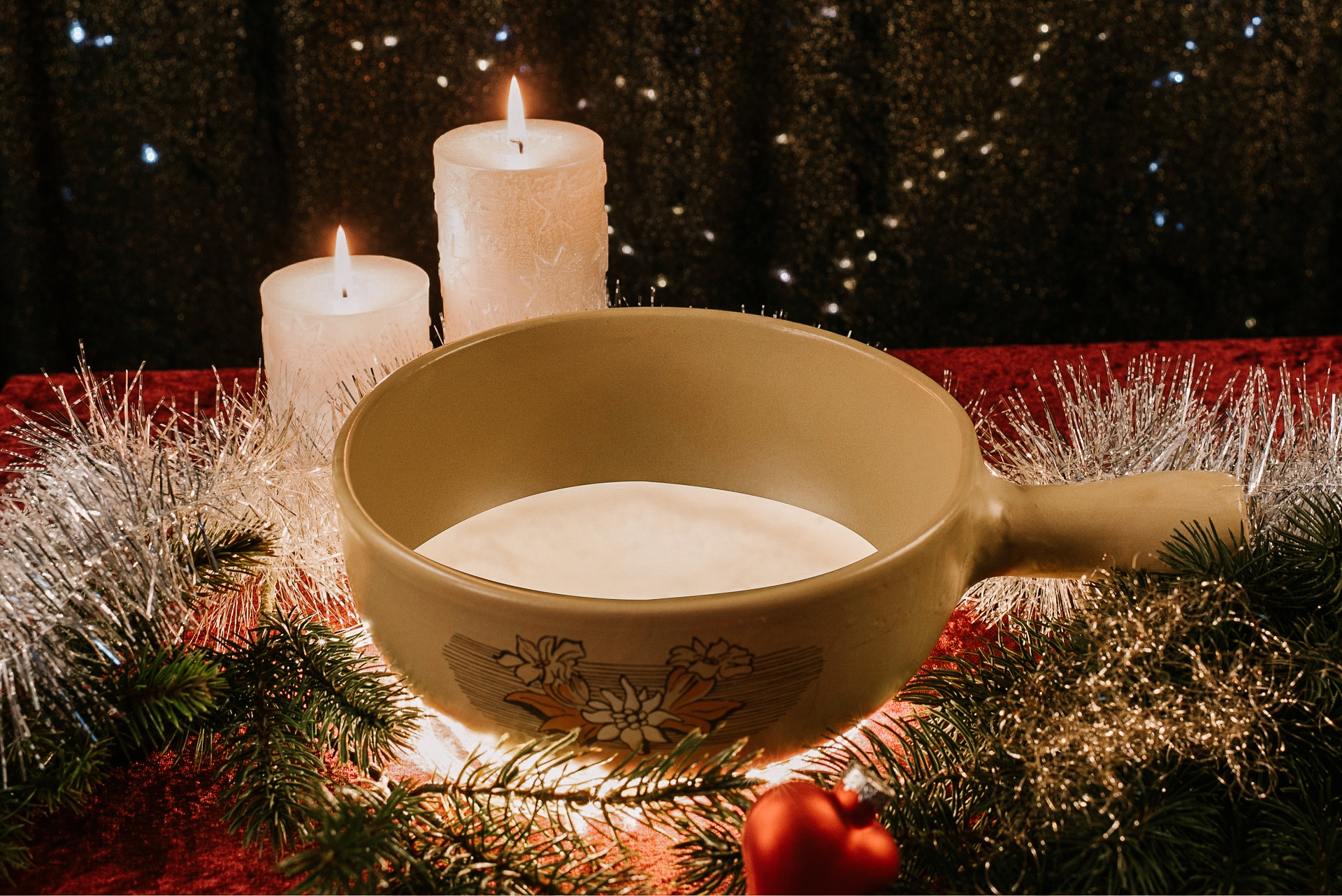 A yellow bowl of cheese fondue with Christmas candles, ornaments and lights surrouding it as a meal in Zermatt for Christmas