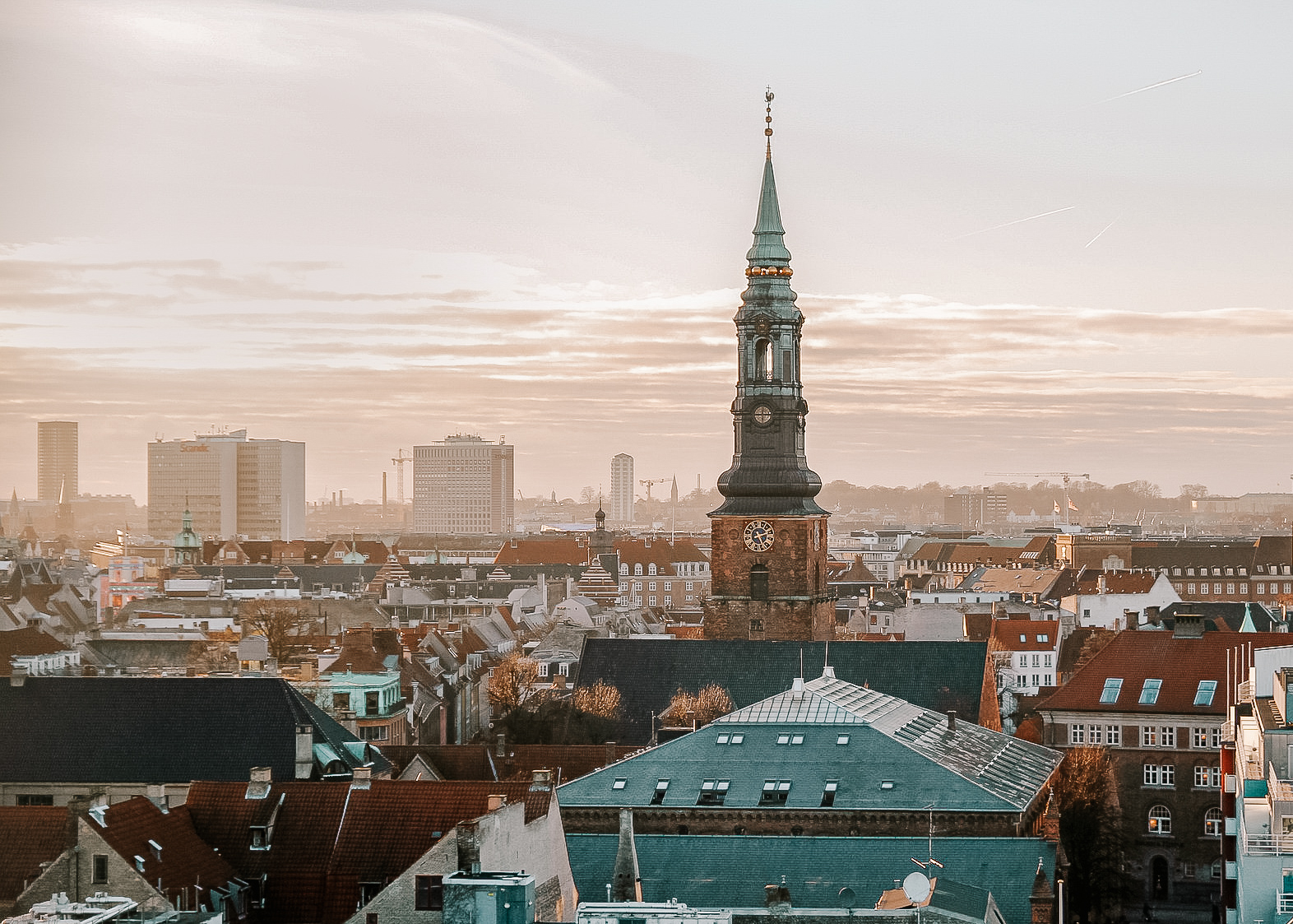 A view of Copenhagen from above, with a view of the church in the foreground and many roofs below, during morning