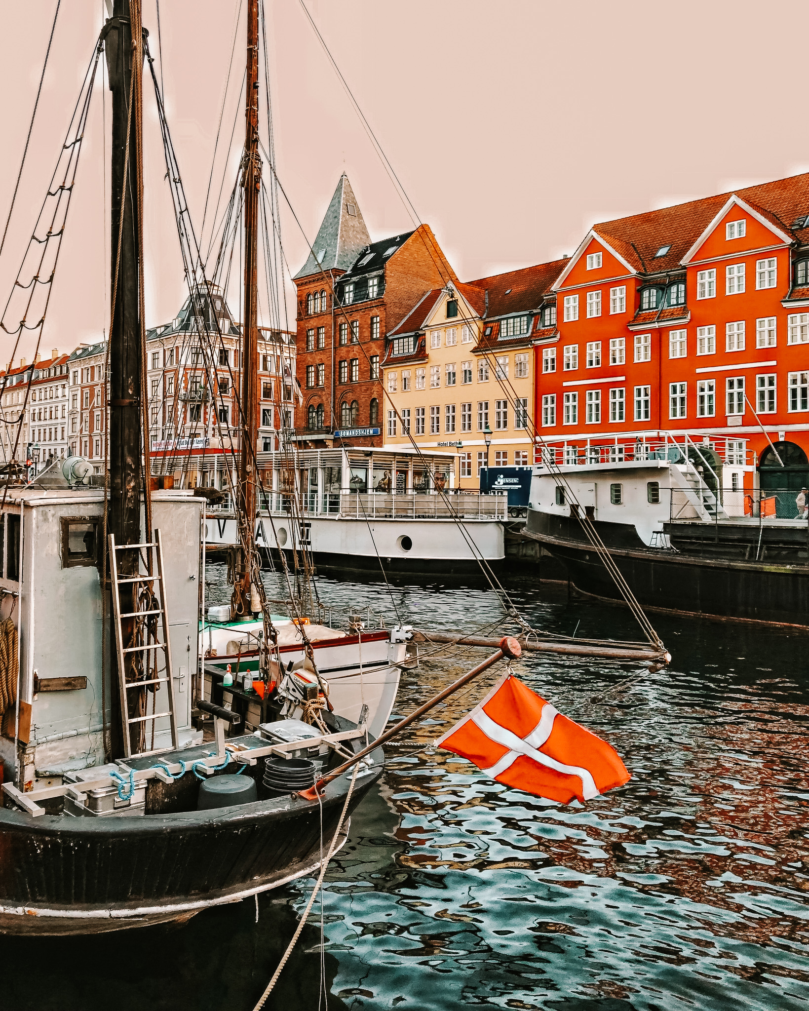 A boat in a canal, with the flag of Denmark on the front-end, with the colorful fisherman houses of Copenhagen in the background.