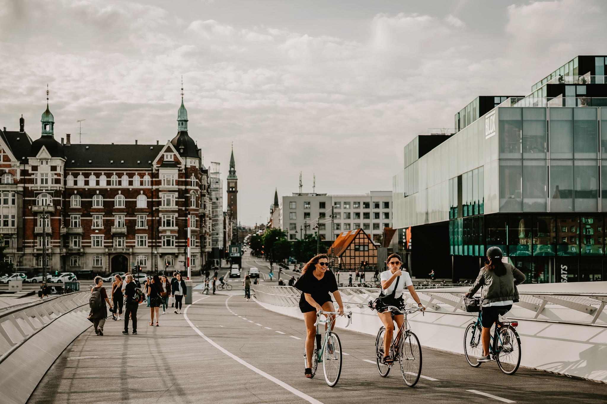 3 cyclists biking in a bike lane in Copenhagen, with pedestrians in the background.