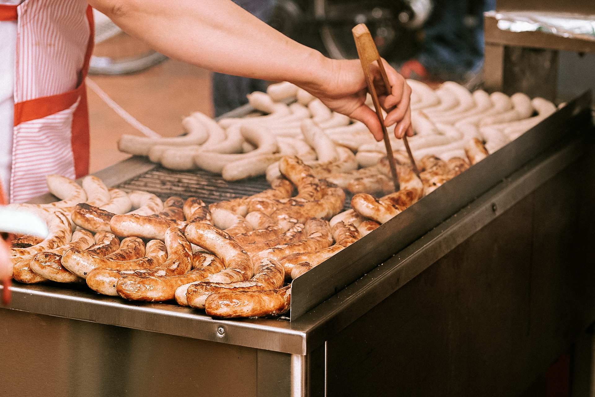 A man cooking bratwursts on a large grill on the streets of St. Gallen