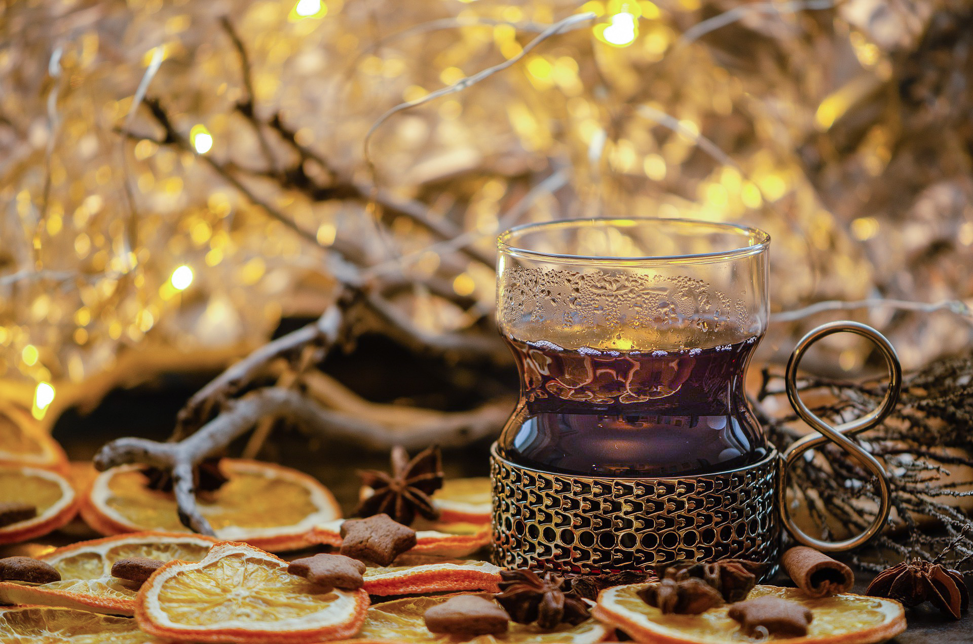 A glass of hot mulled wine on some slices of orange, anise stars and with Christmas lights in the background