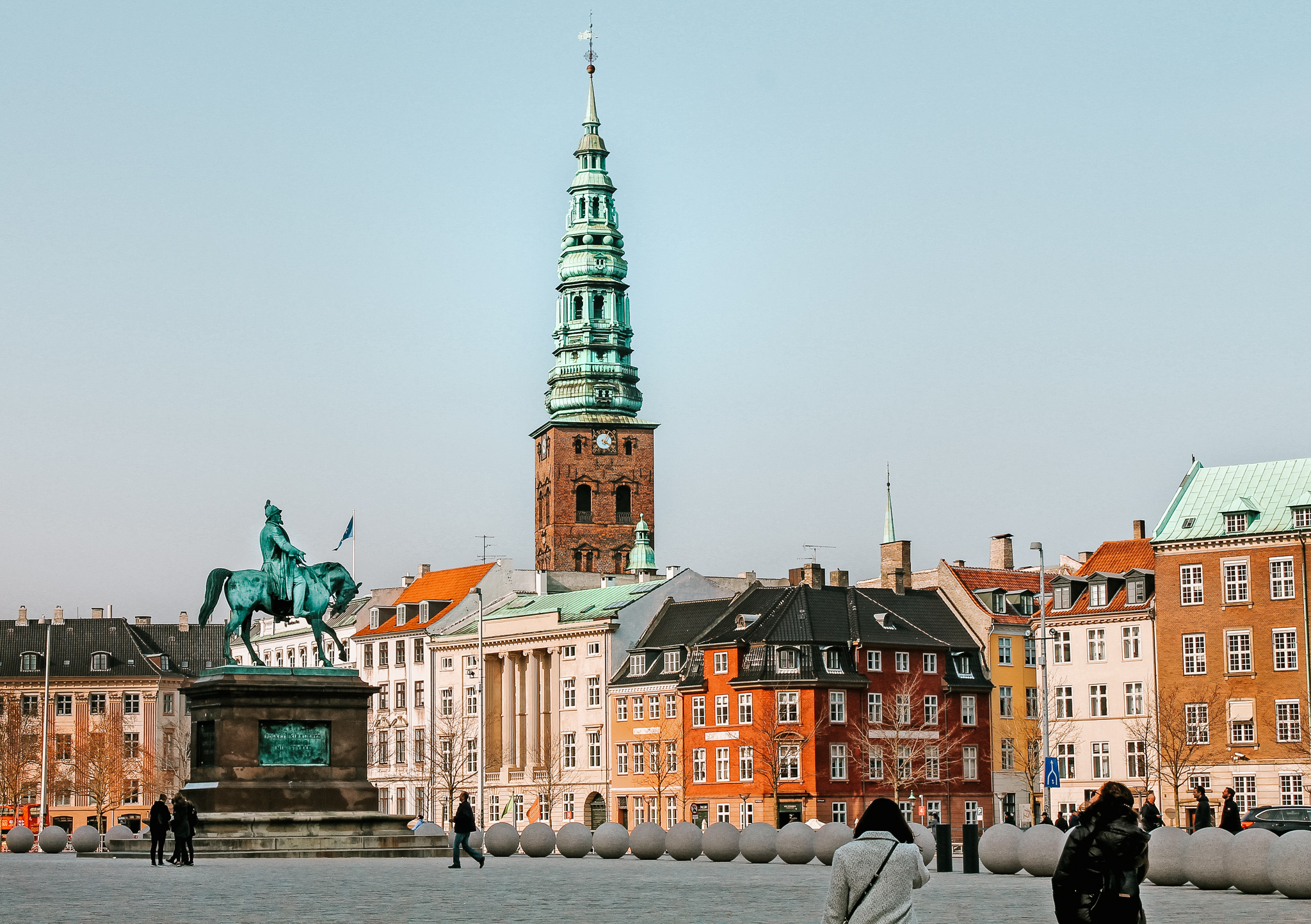 Christiansborg Palace's green, copper tower above colorful buildings in a square in Copenhagen.