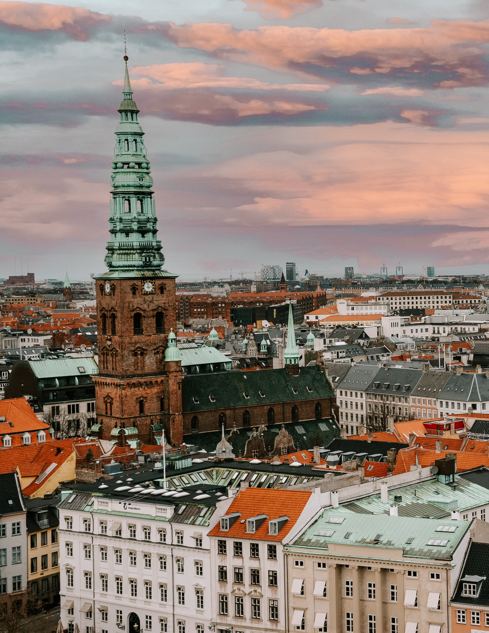 A view of Copenhagen from above, with a view of the church in the foreground and many roofs below, during sunset.