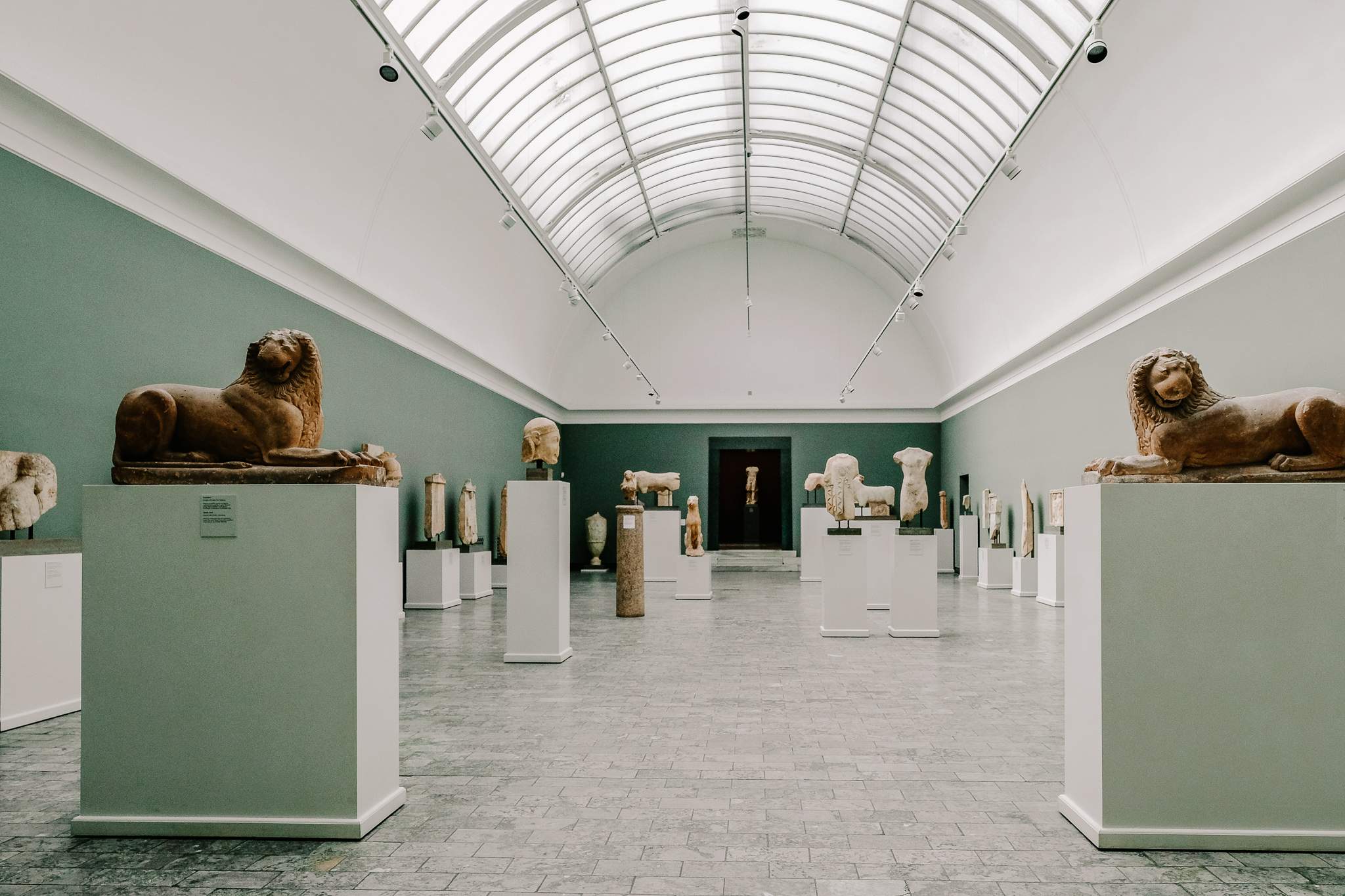 A picture of some lion sculptures in a museum in Copenhagen, in a room with green paint and a curved ceiling made of glass letting in a lot of light.