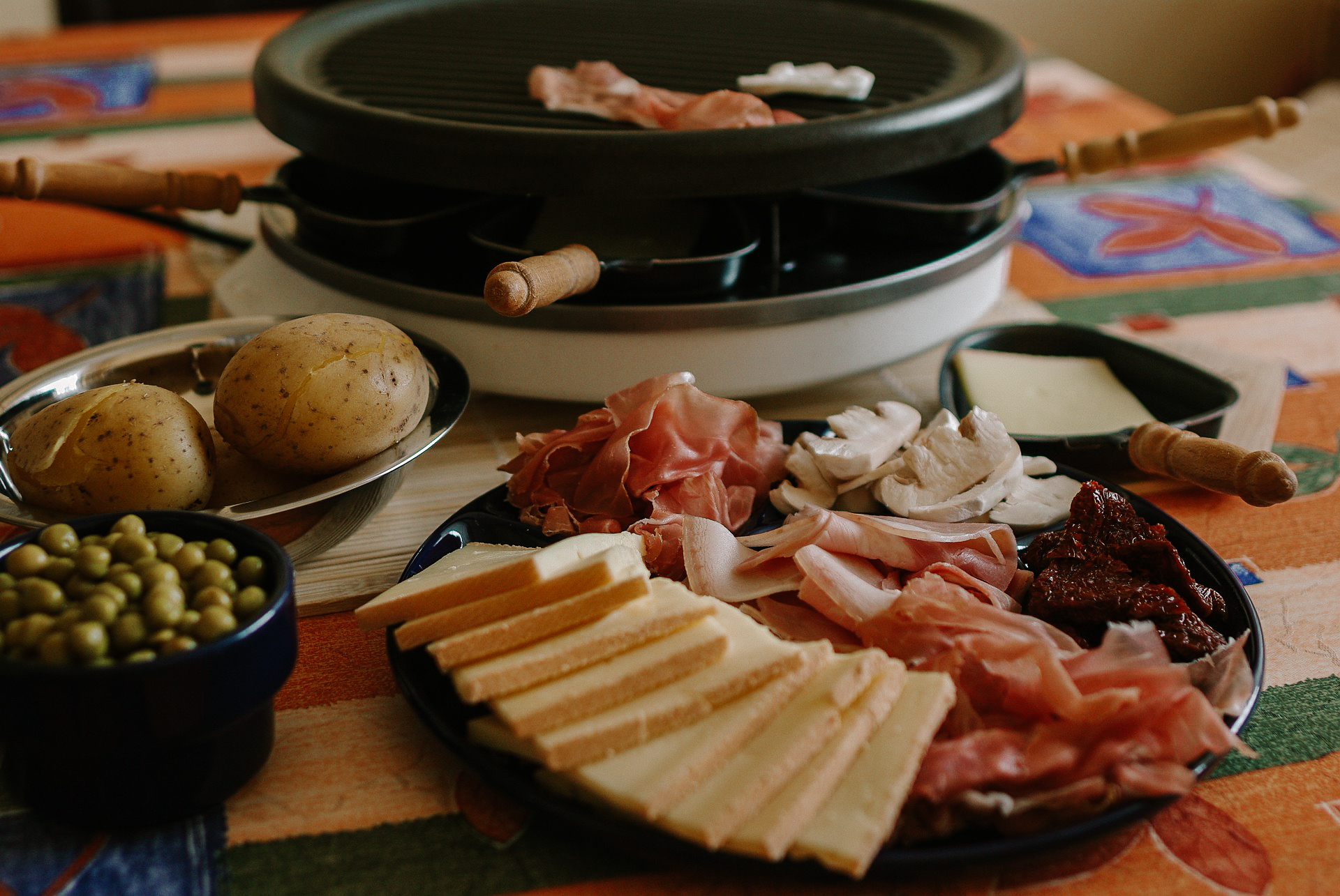 A meal in Zermatt for Christmas made up of a plate of charcuterie meat, raclette cheese, mushrooms, peas, and potatoes in front of a raclette grill