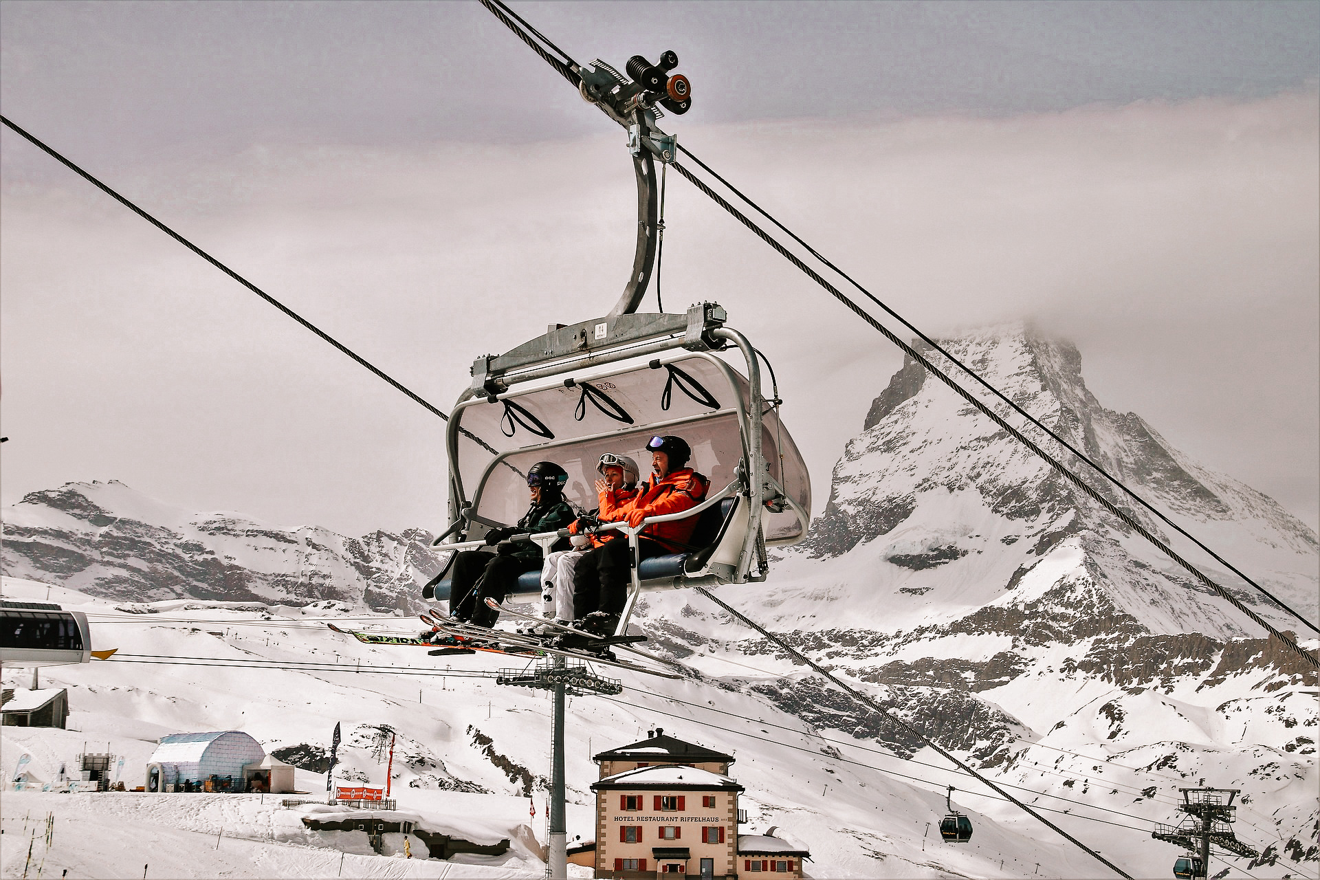 A single ski lift taking three people up the side of the mountain, with Matterhorn peak in the background with the tip covered in clouds.