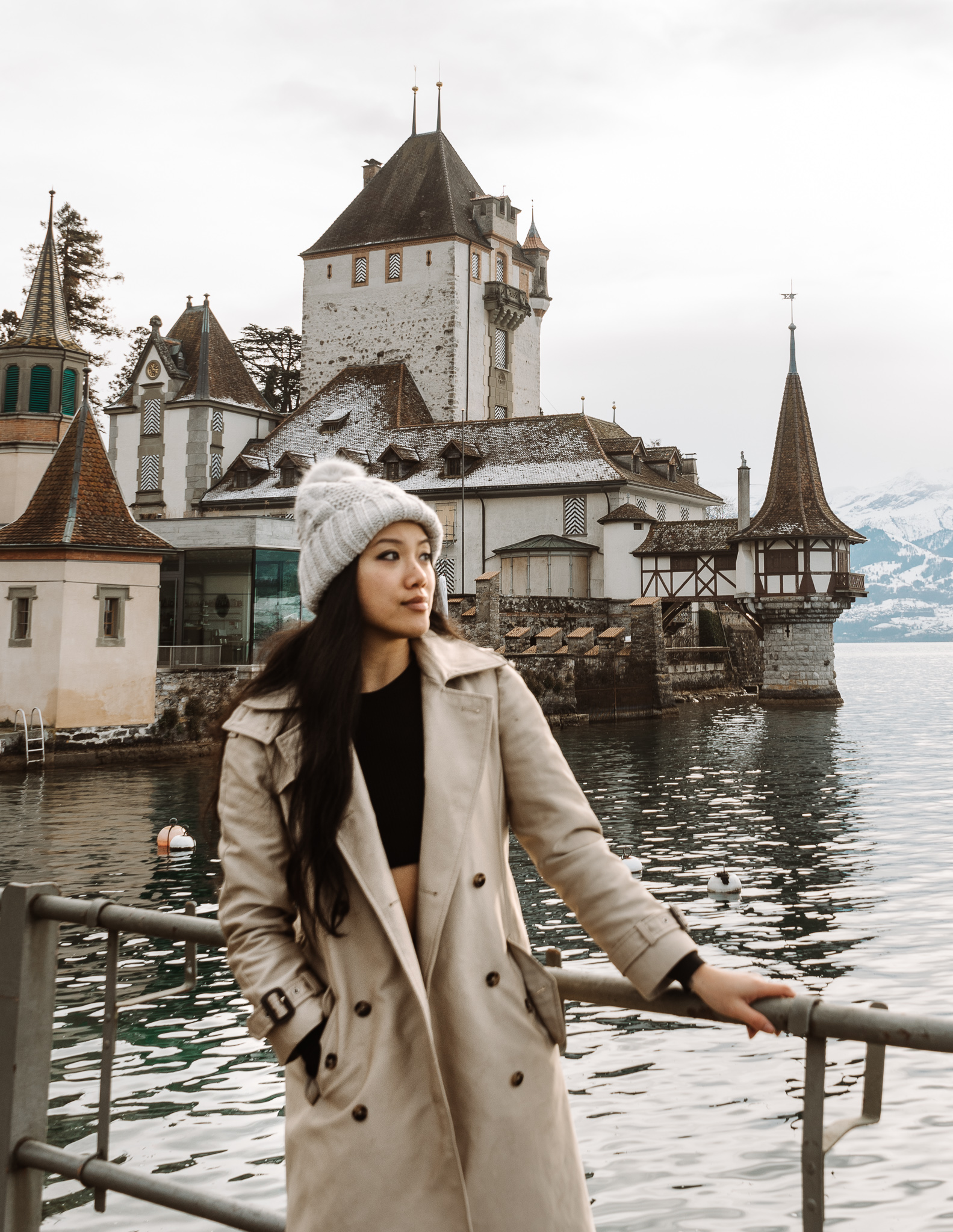 A woman stading in front of Oberhofen Castle, a medieval style castle right on a lake in winter.