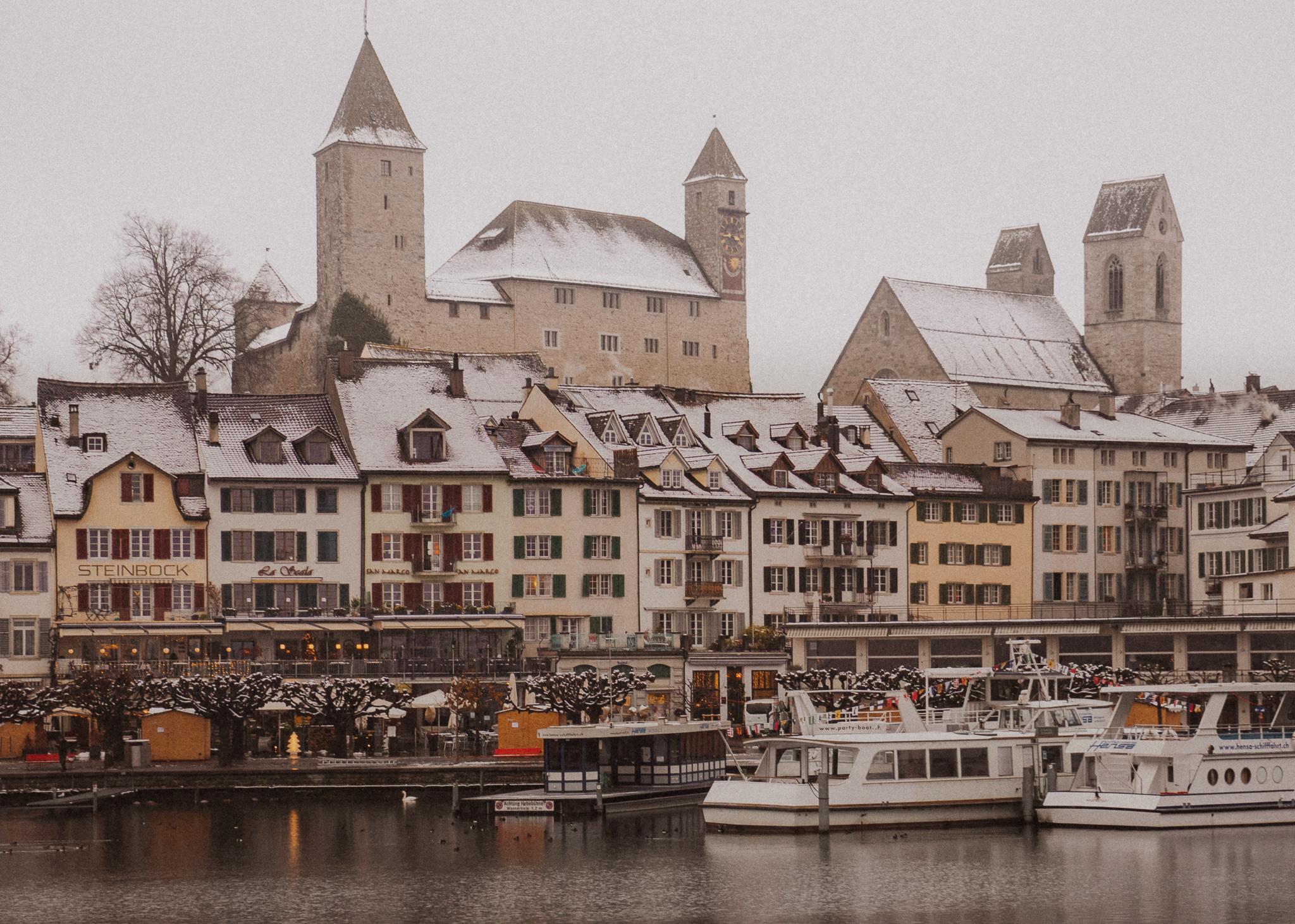 Rapperswil castle and the town below it on a winter day with snow on the roofs and the lake in front of it