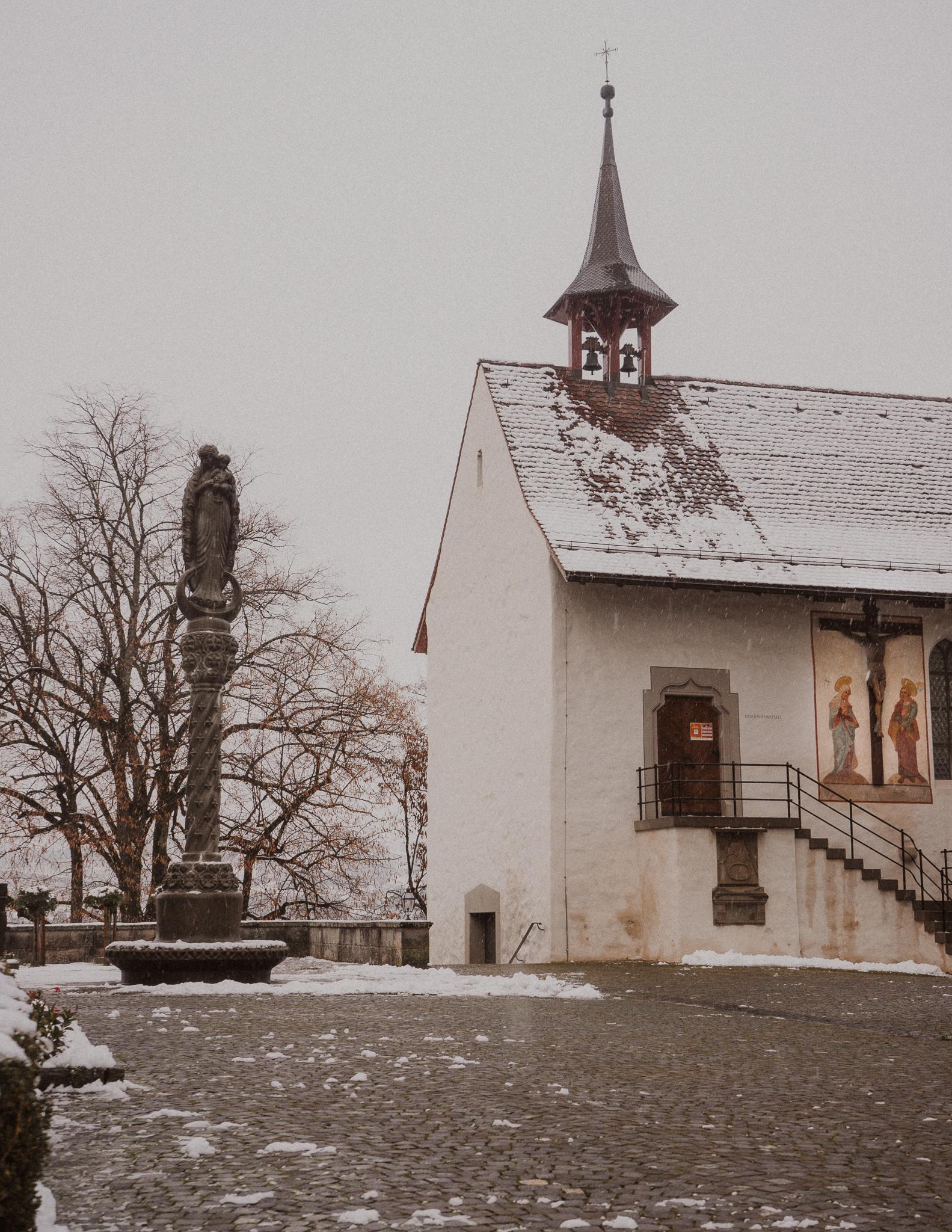 A historic church with snow and a colorful religious fresco, in a cobbled square in Rapperswil 