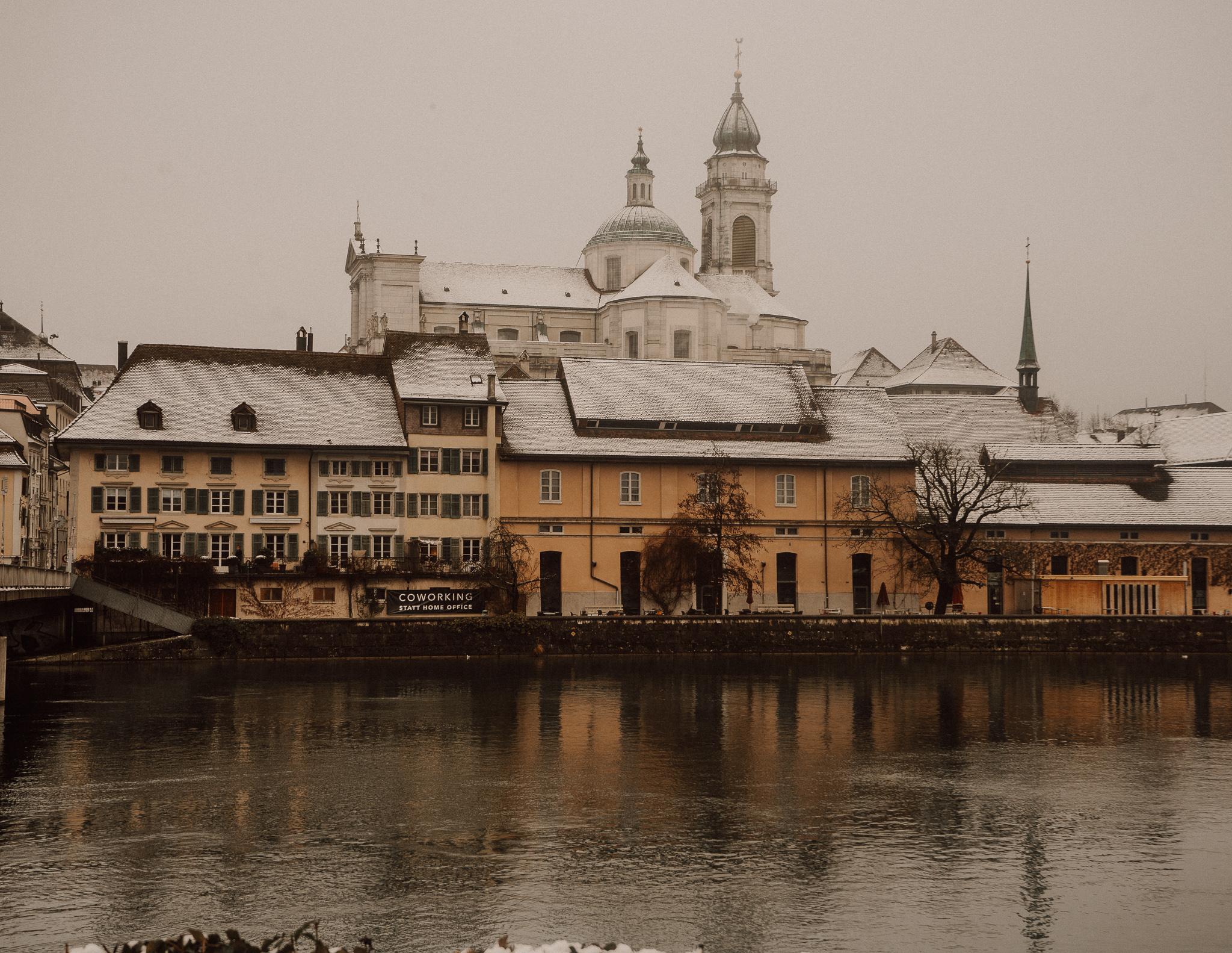 A view of Solothurn village in Switzerland across the river with snow on the buildings roofs on a cloudy day
