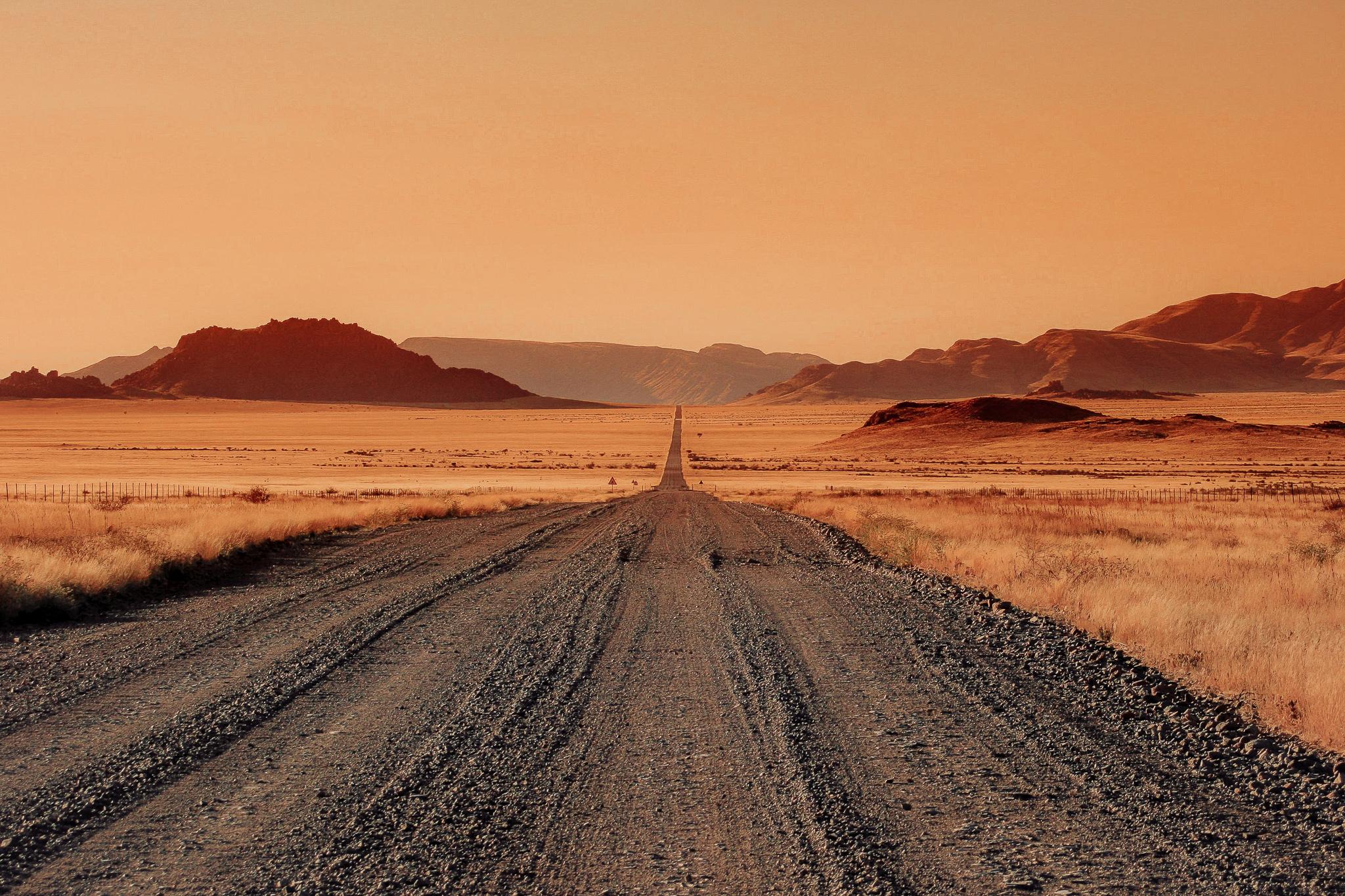 A deserted gravel road encountered during a Namibia self drive with red mountains and canyons in the far distance