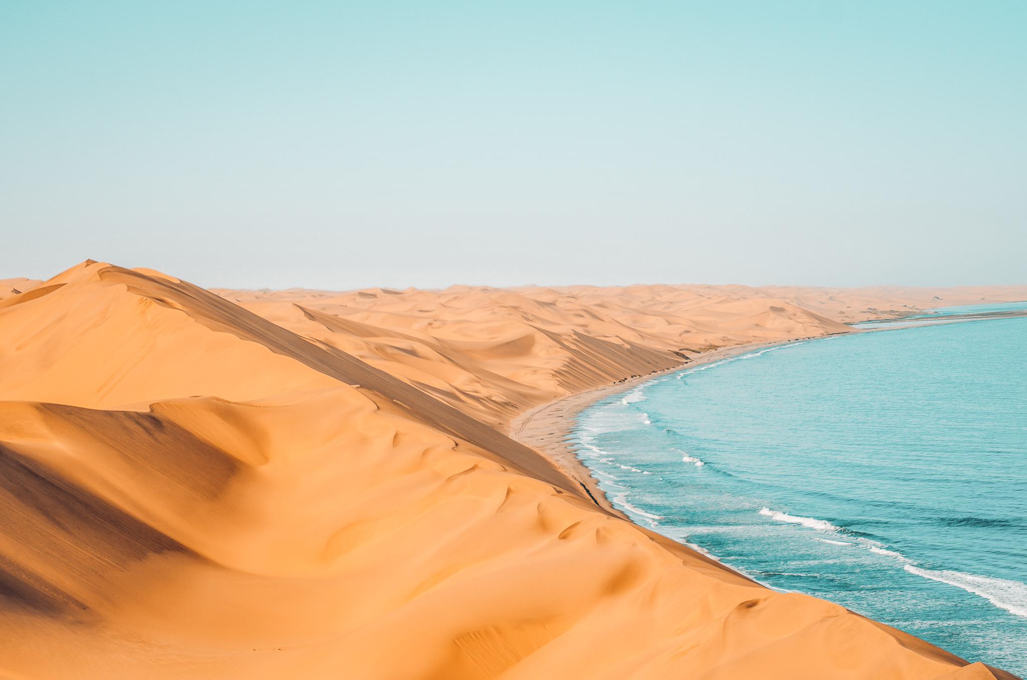 orange sand dunes touching the blue ocean below