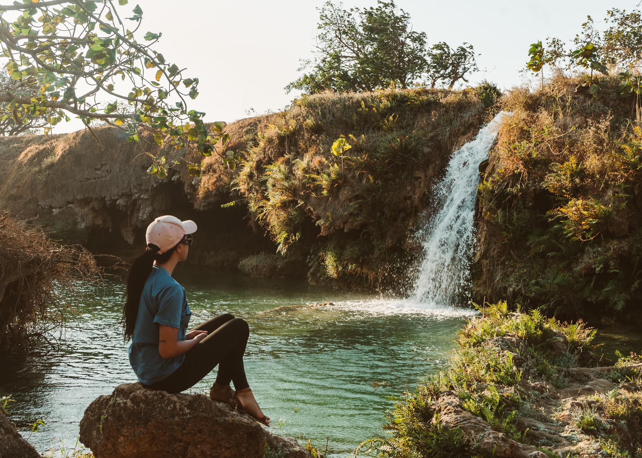 A girl sitting by a waterfall in Selalah, Oman