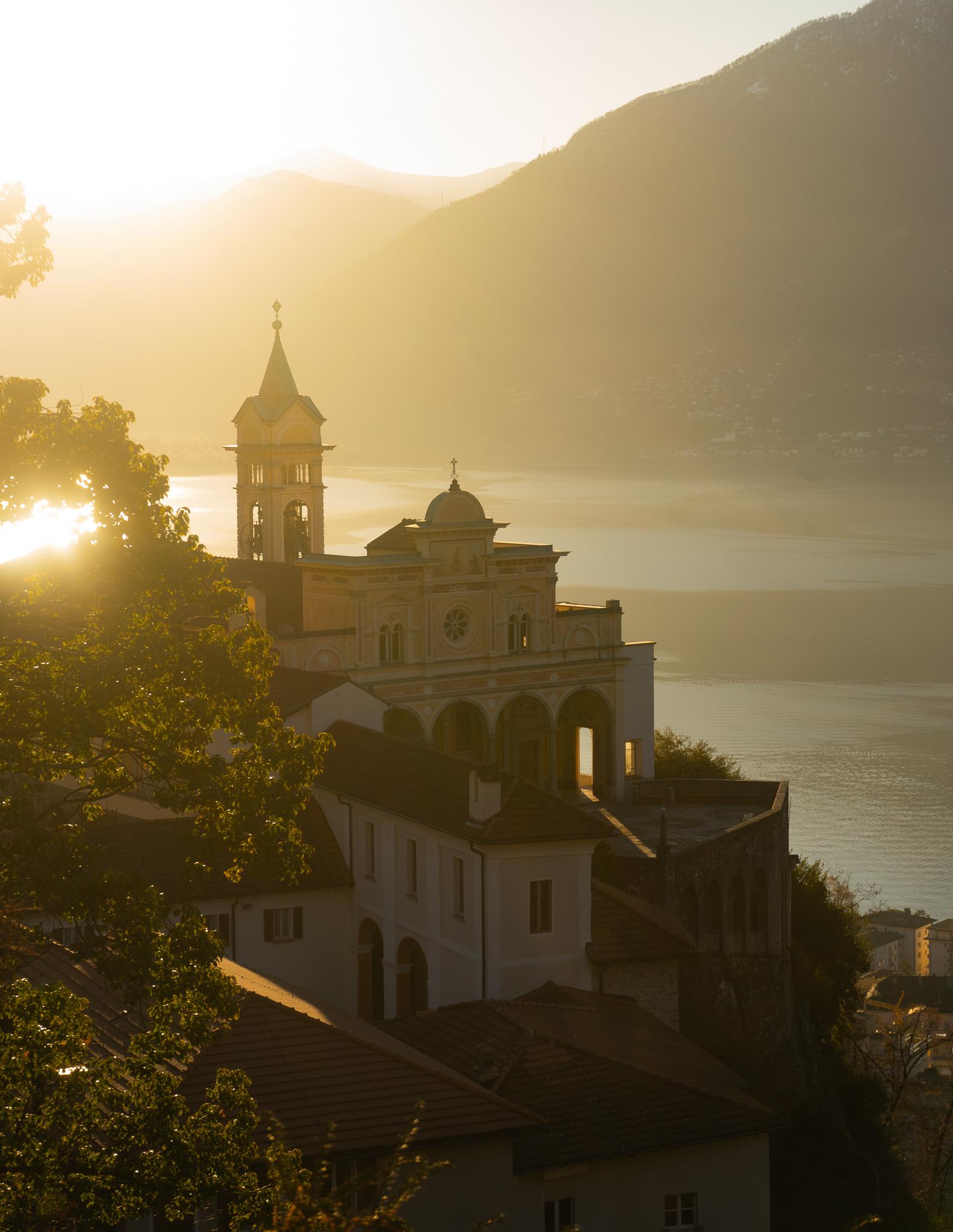 View of Madonna del Sasso church in Locarno at sunrise, with the sun and lake behind