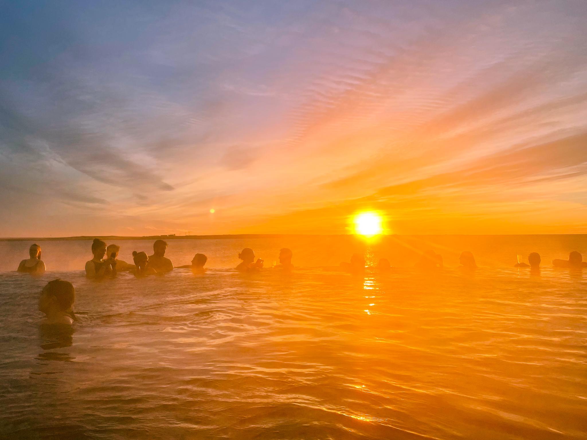 many people in the Sky Lagoon geothermal bath during sunset in Iceland overlooking the sea