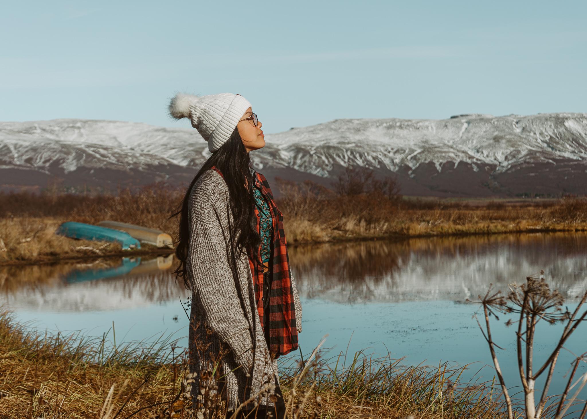 a woman standing in front of snowy mountains and Laugarvatn Lake in Iceland