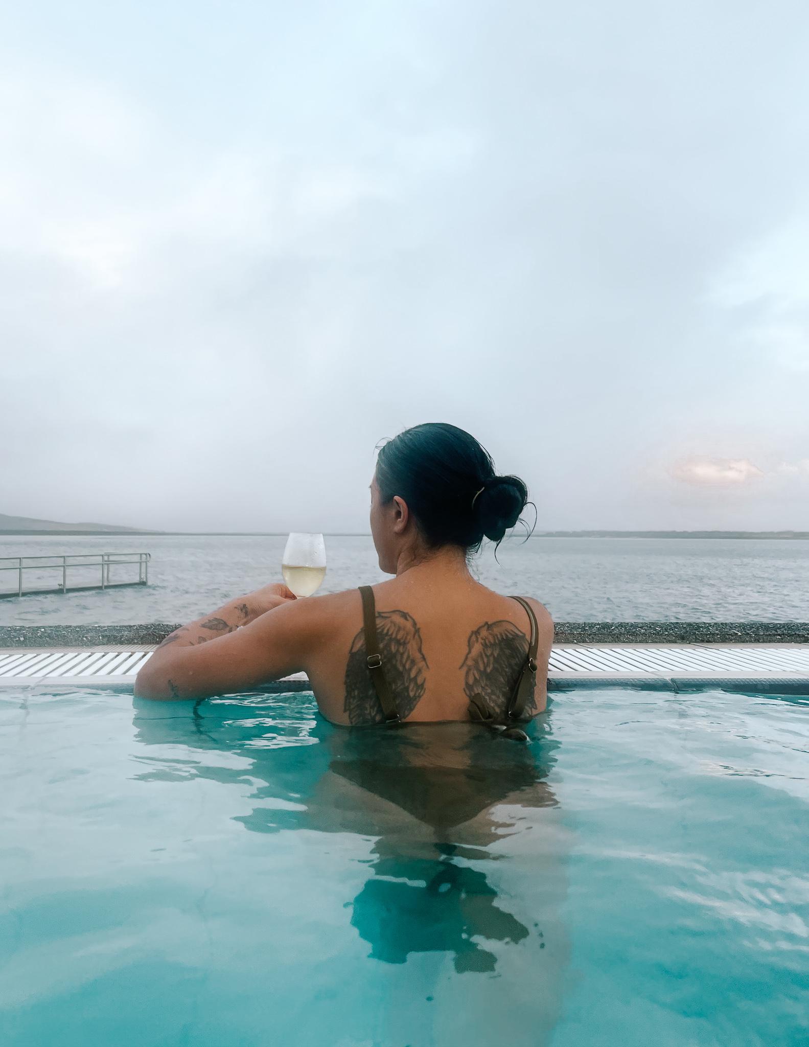 A woman holding a glass of white wine in Fontana Spa overlooking Laugarvatn Lake in Iceland