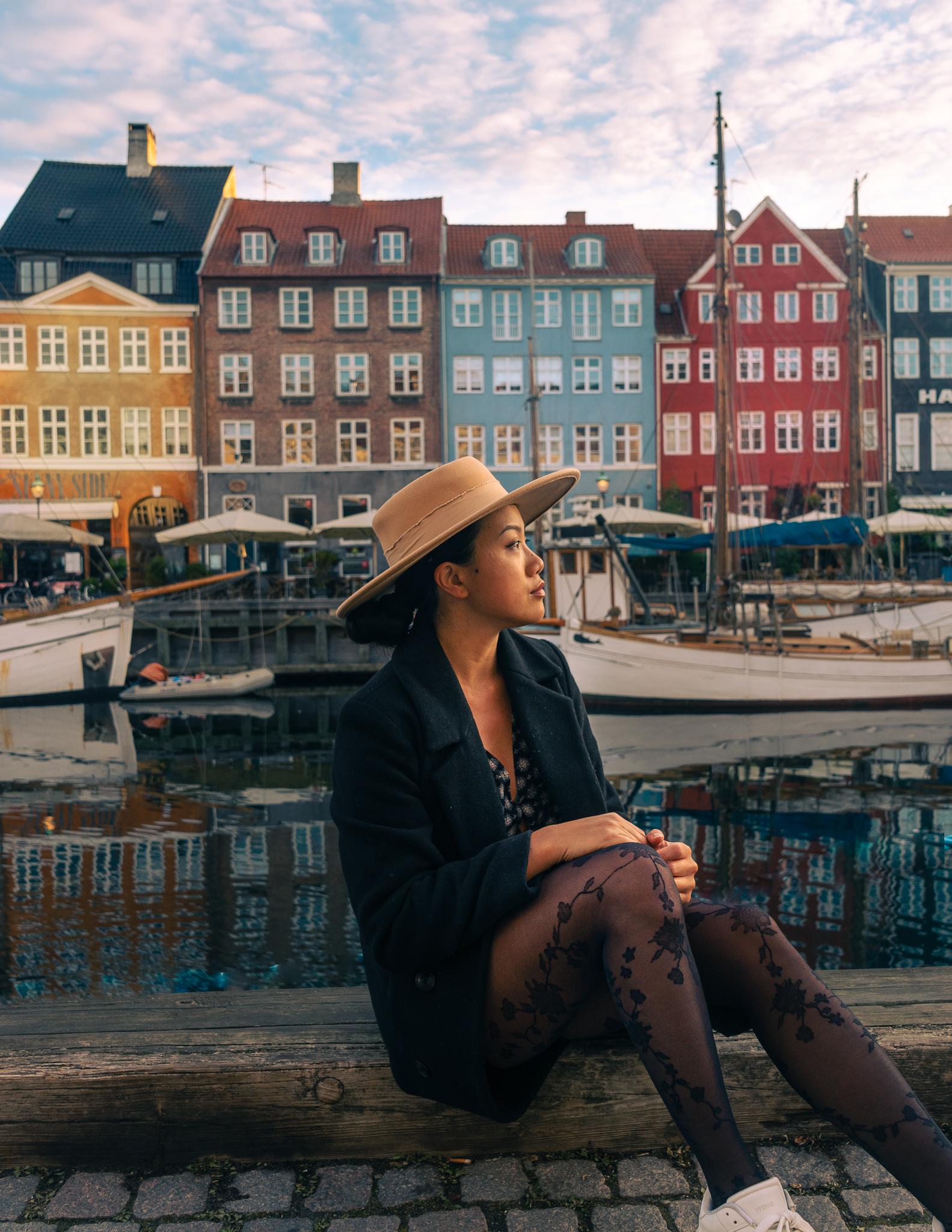 A girl sitting in front of colorful fisherman houses in Copenhagen, Denmark.