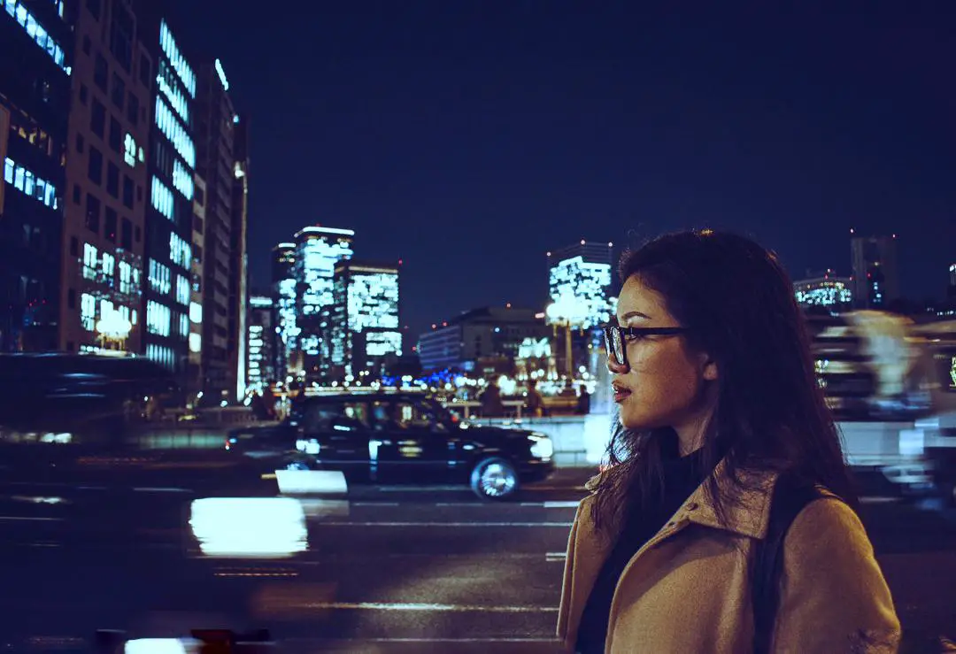 A girl standing in front of moving traffic and buildings at night in Osaka, Japan.